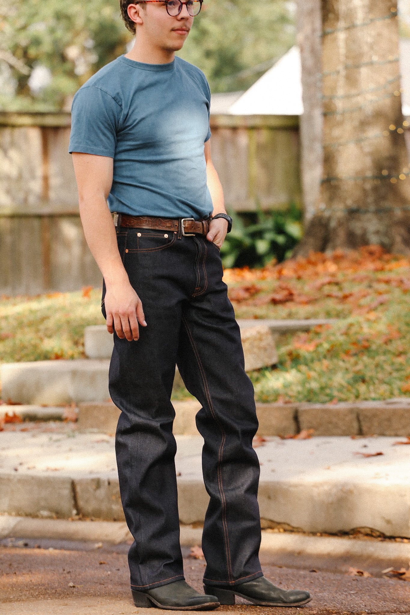 Man wearing wide straight 16.5oz Kaisen Indigo denim jeans with brown belt and blue t-shirt outdoors