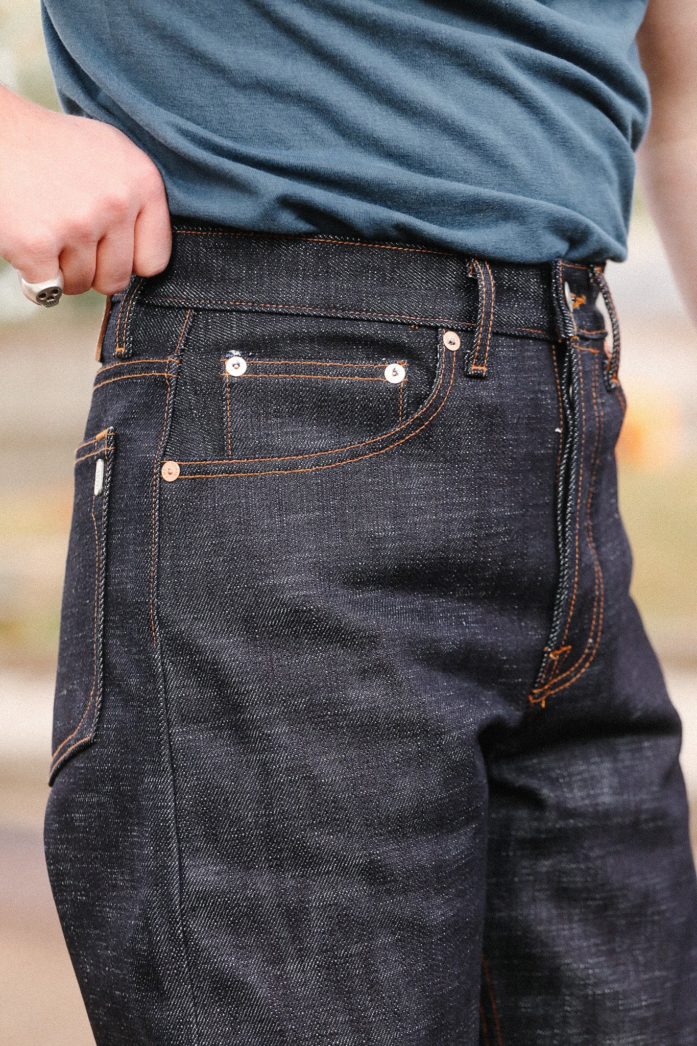 Close-up of person wearing dark indigo wide straight jeans with orange stitching and silver rivets