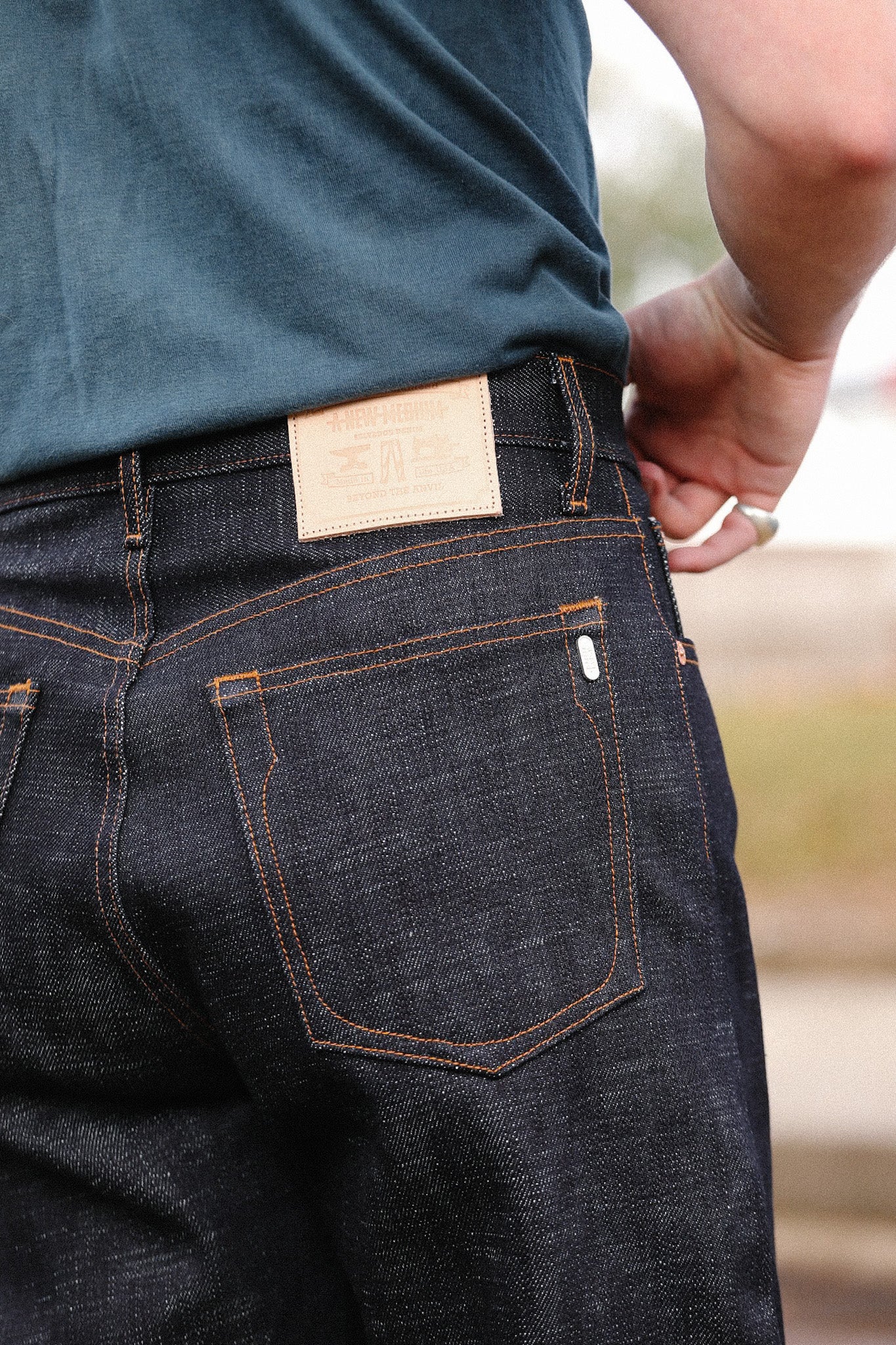 Close-up of a person wearing dark indigo wide straight jeans with orange stitching and a leather patch at the back waistband