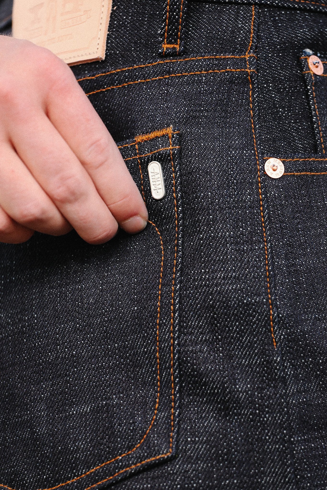 Close-up of hand touching dark indigo denim jeans pocket with orange stitching and metal rivets