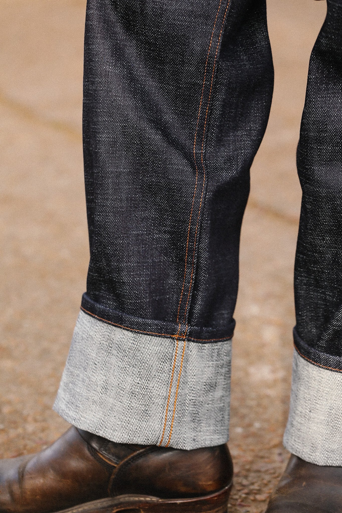 Close-up of wide straight 20oz indigo selvedge jeans cuffed over brown leather boots on concrete surface