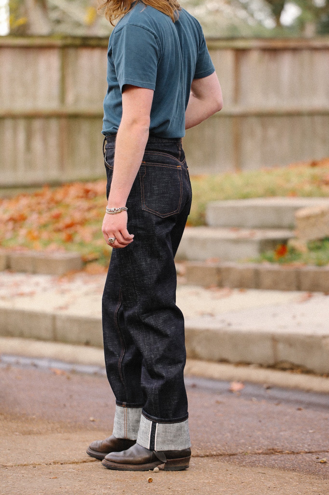 Side view of person wearing dark indigo wide straight jeans with rolled cuffs and brown leather boots outdoors