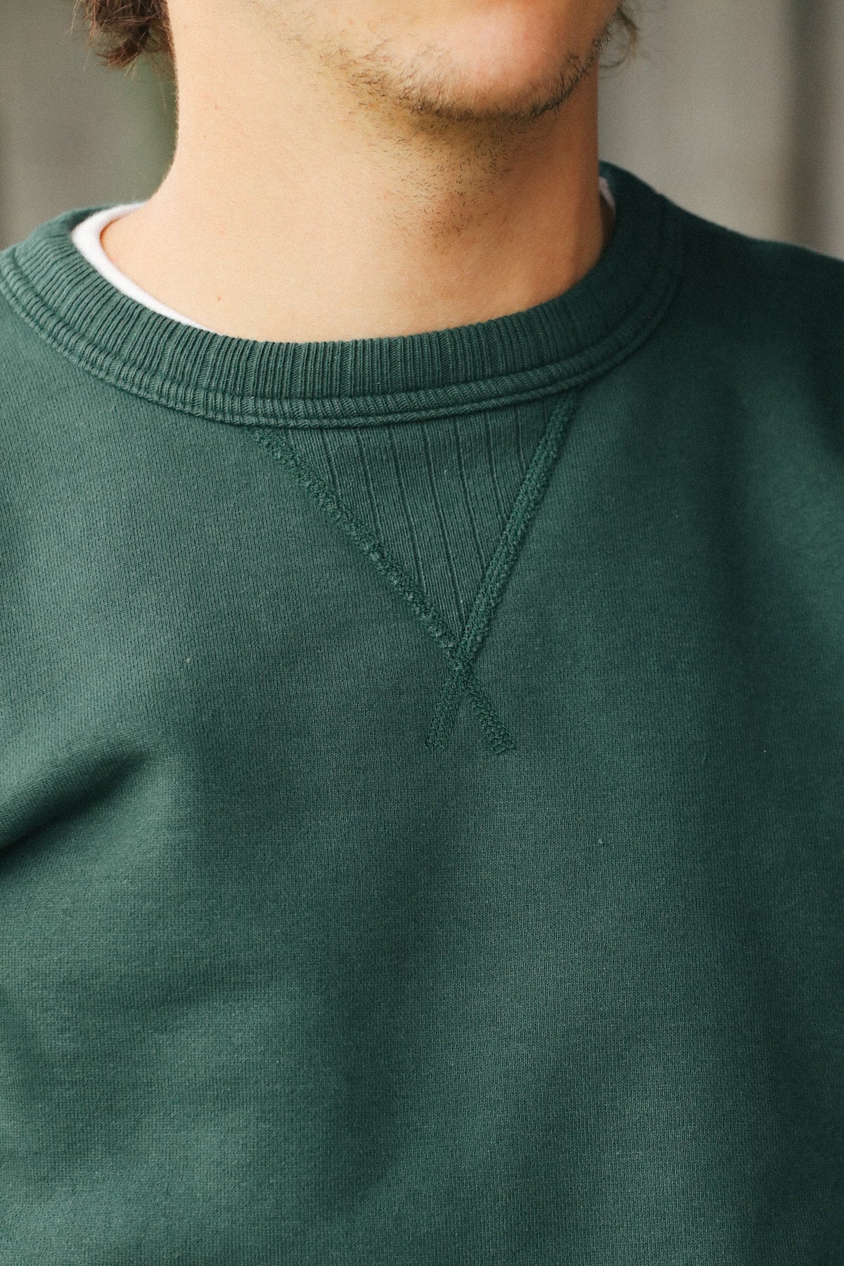 Close-up of a person wearing a dark forest green crewneck sweatshirt, showing the ribbed collar and textured chest fabric.