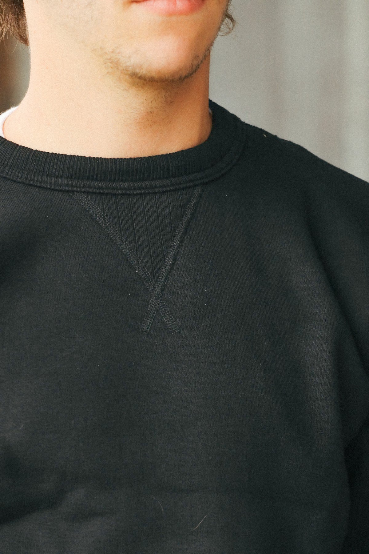 Close-up of a person wearing a black crewneck sweatshirt, showing the ribbed collar and chest seam details.