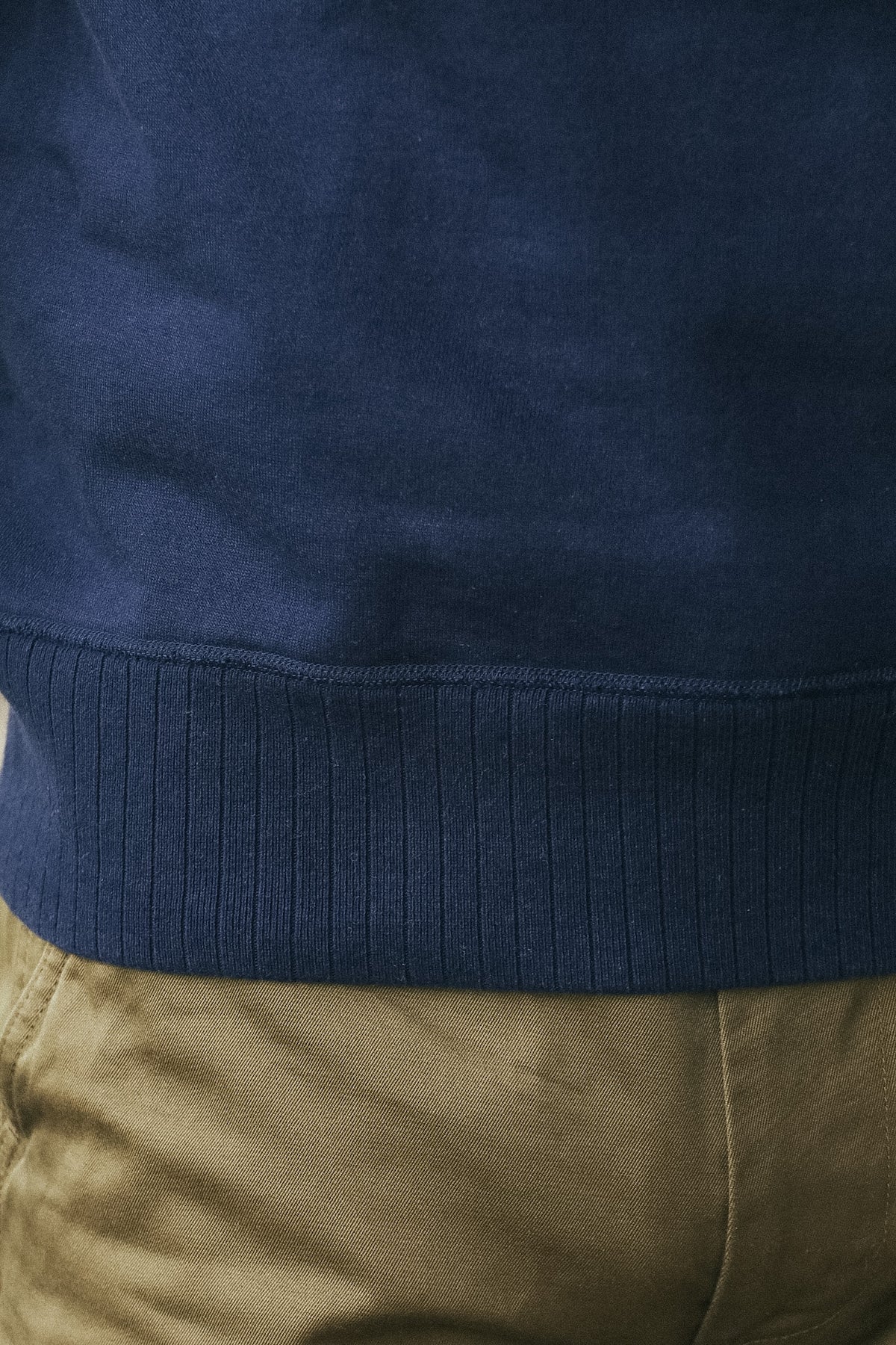 Close-up of a navy blue ribbed knit top worn with tan pants, showing the texture and hem detail.