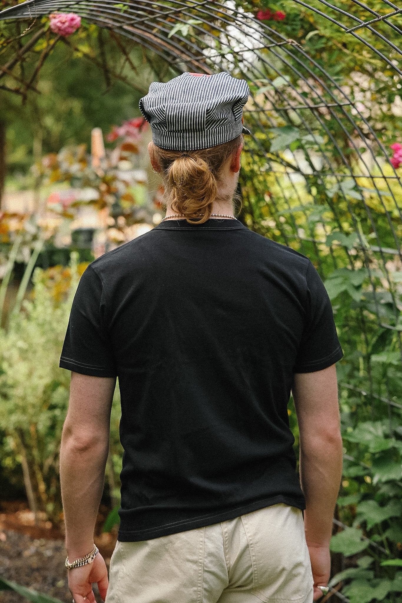 Person wearing a black t-shirt and striped cap in a garden setting