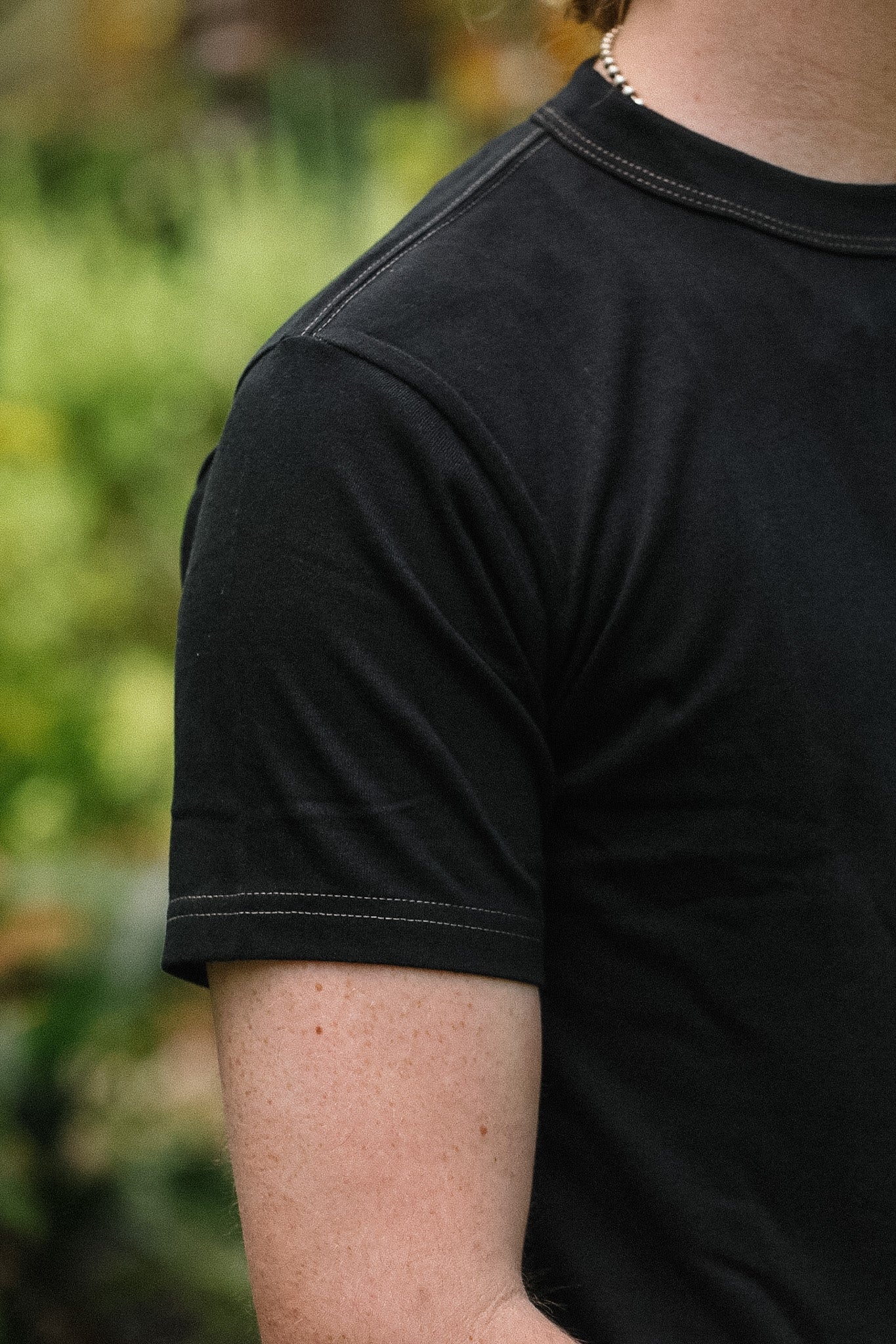 Person wearing a black t-shirt with a blurred natural background