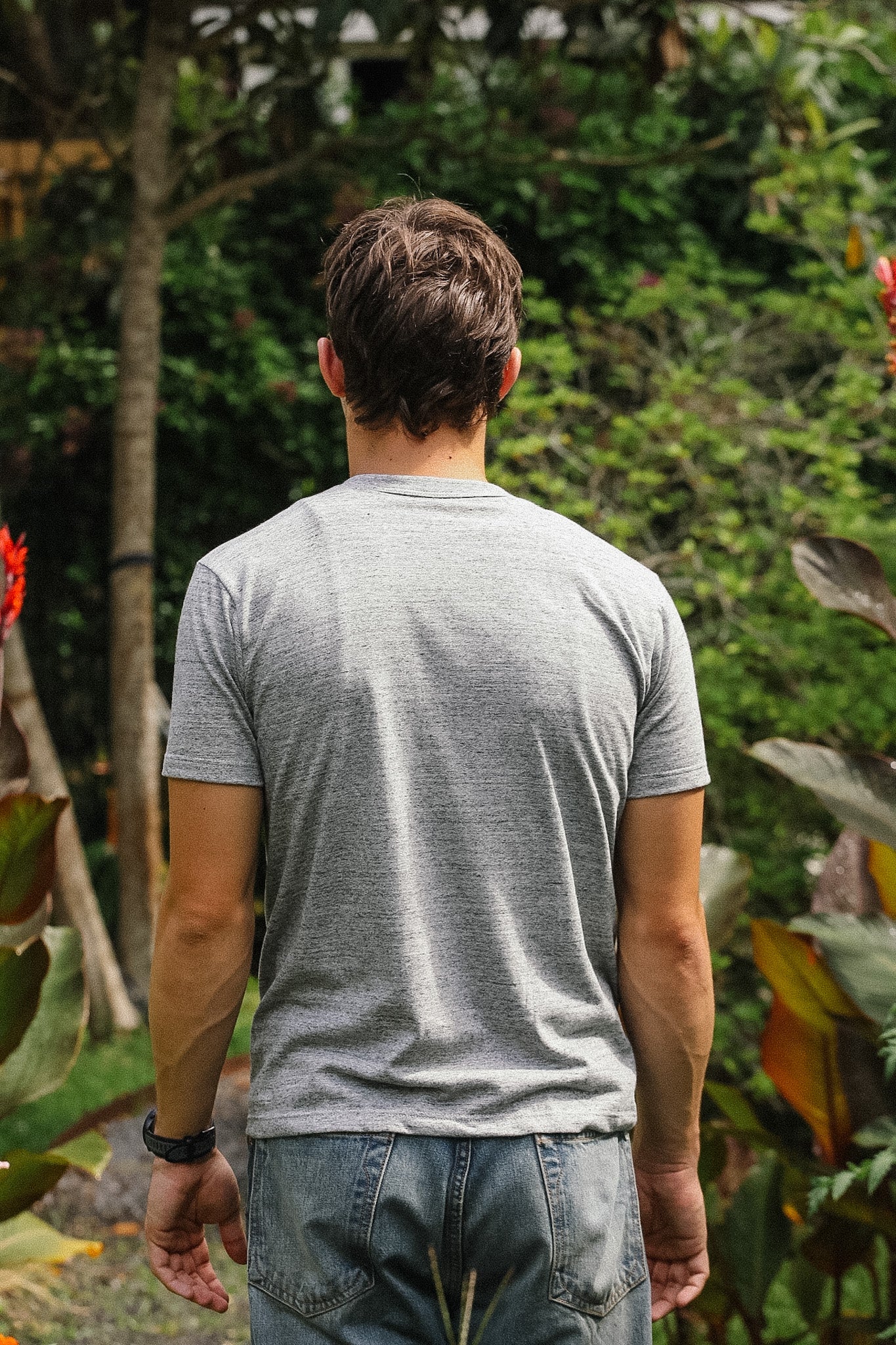Man wearing a gray t-shirt and jeans standing in a garden with greenery.
