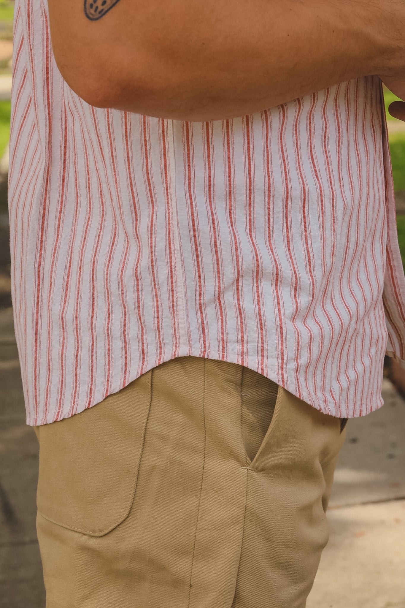 Person wearing a red and white striped shirt and beige pants with a brown bag.