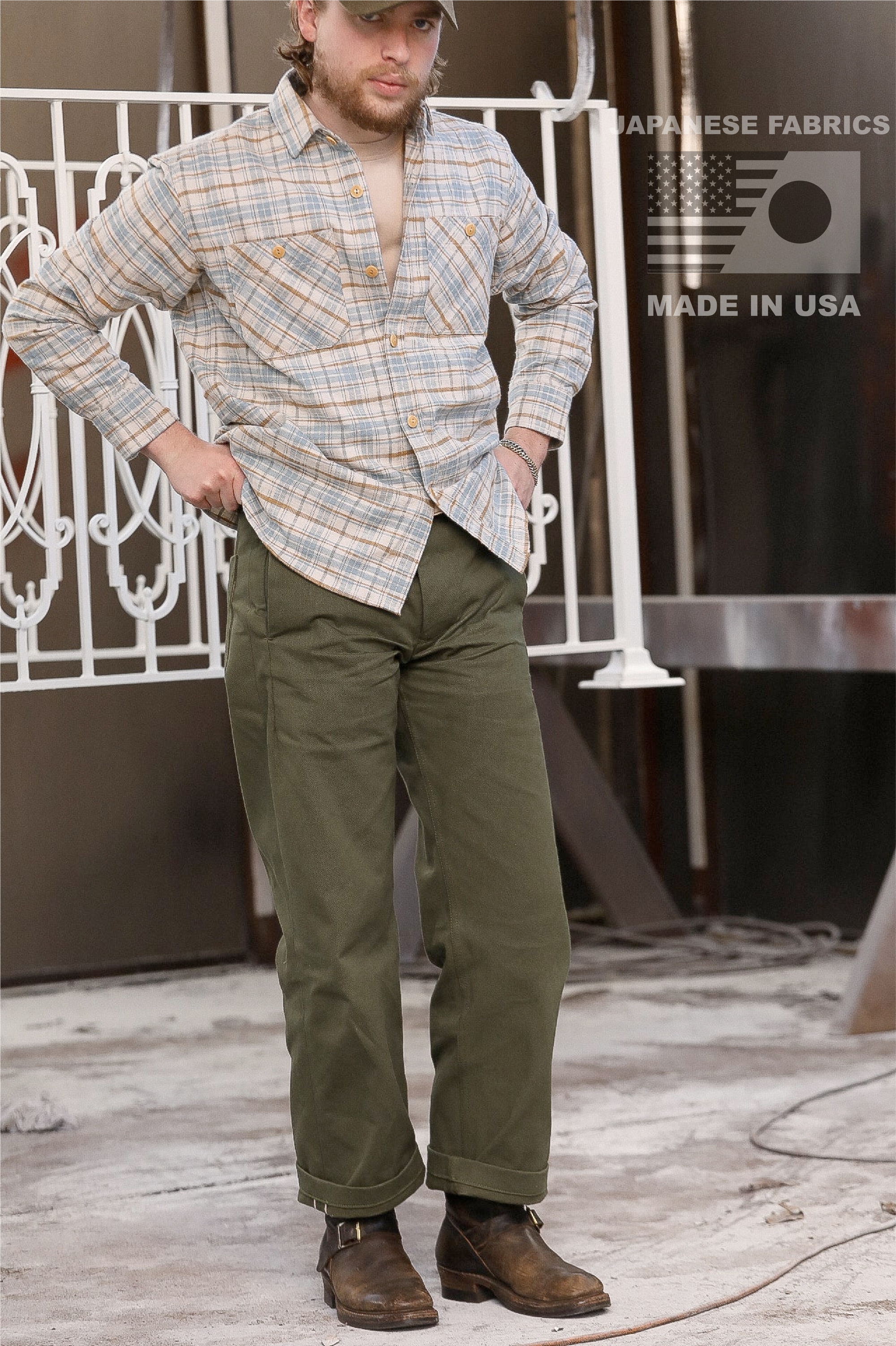 Model wearing olive chino pants and plaid shirt with boots in industrial setting with Japanese fabrics and Made in USA text
