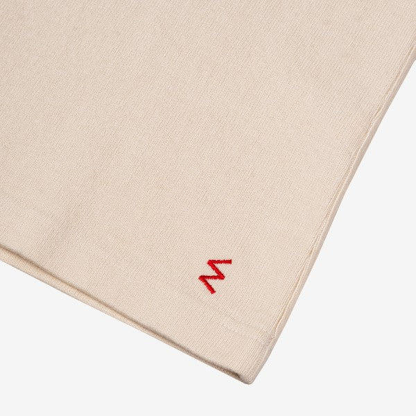Beige fabric clothing detail with small red embroidered zigzag logo on corner from Iron Shop Provisions