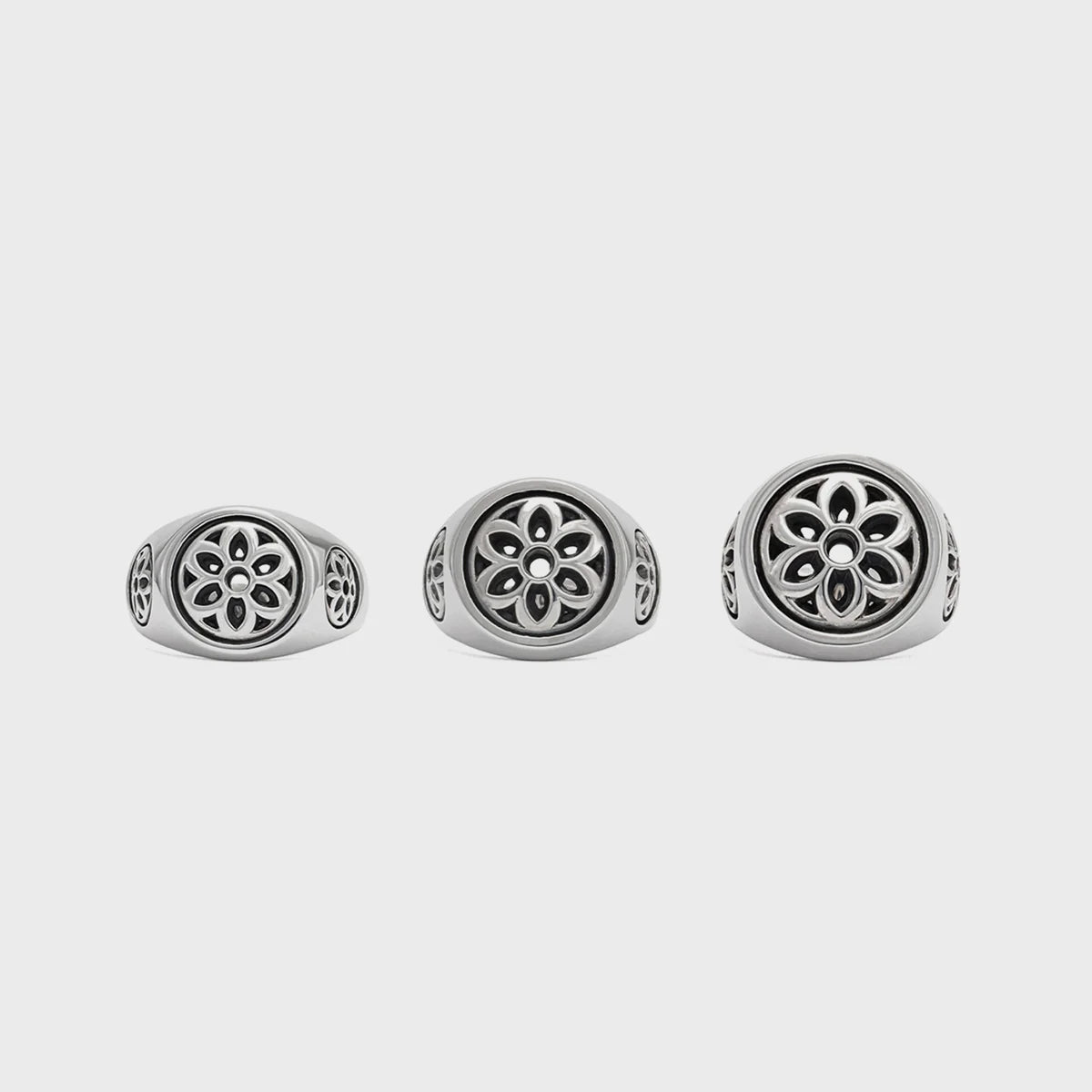 Three silver rings with cutout floral designs in varying sizes on plain background