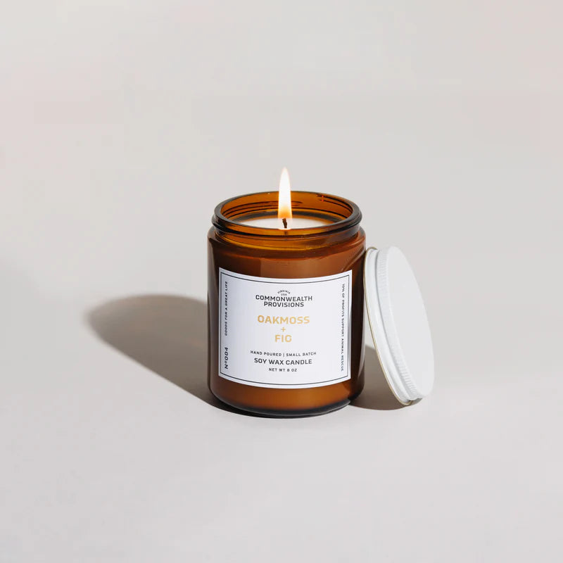 Lit Oakmoss and Fig soy wax candle in amber glass jar with white lid, minimalist background