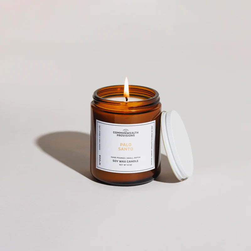 Lit Palo Santo soy wax candle in amber glass jar with white label and lid on side