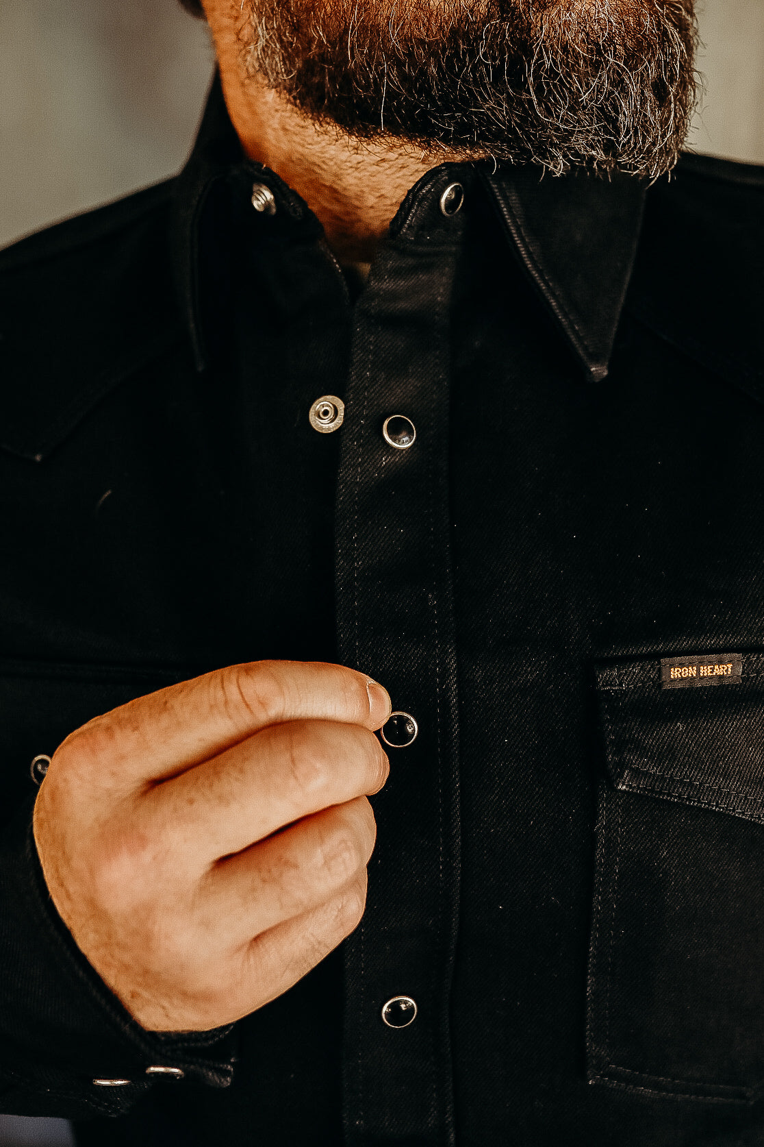 Close-up of a man with beard fastening black Iron Heart jacket with metal snap buttons