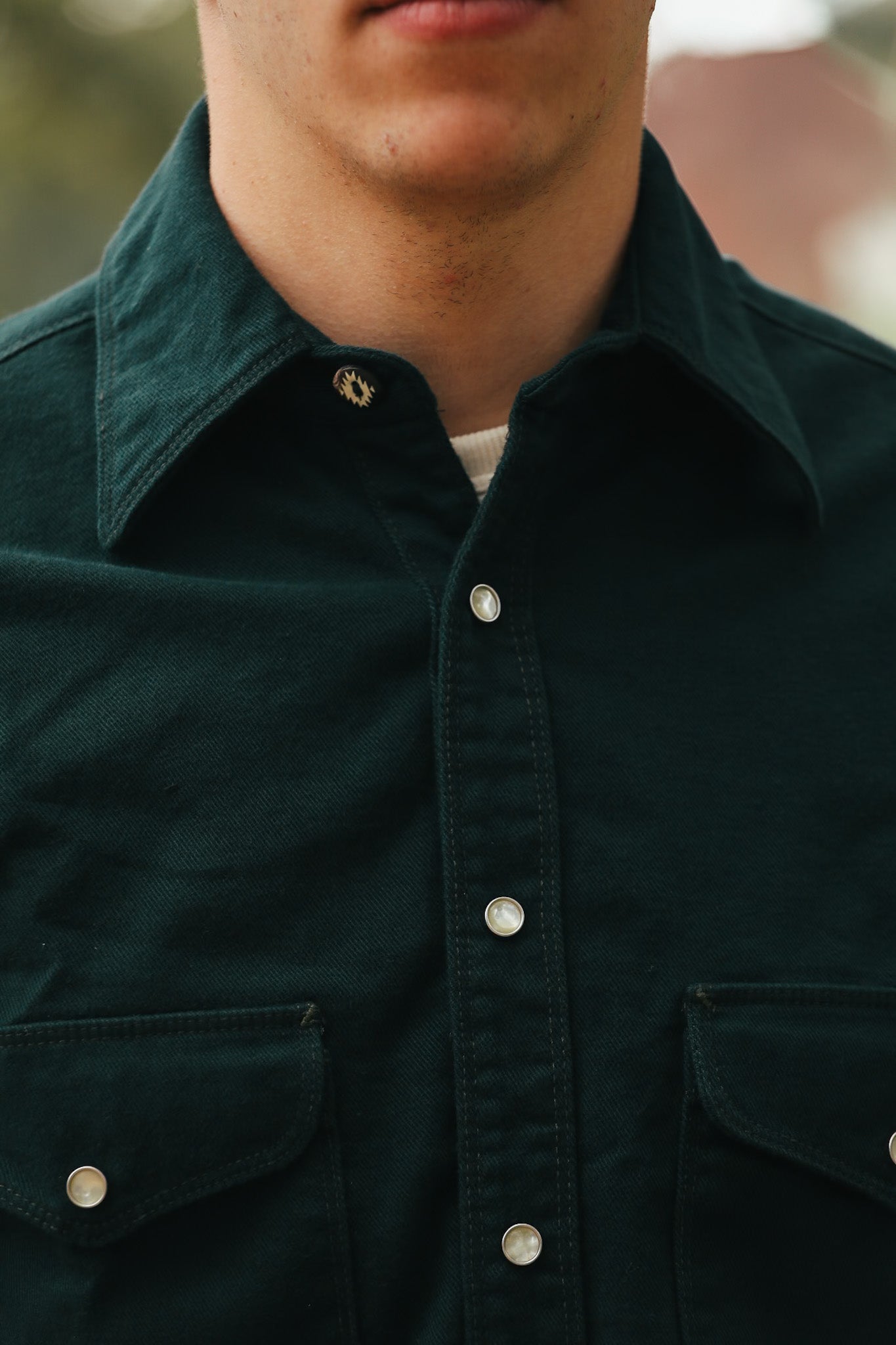 Close-up of a person wearing a dark green button-up shirt with pearl snap buttons and flap pockets