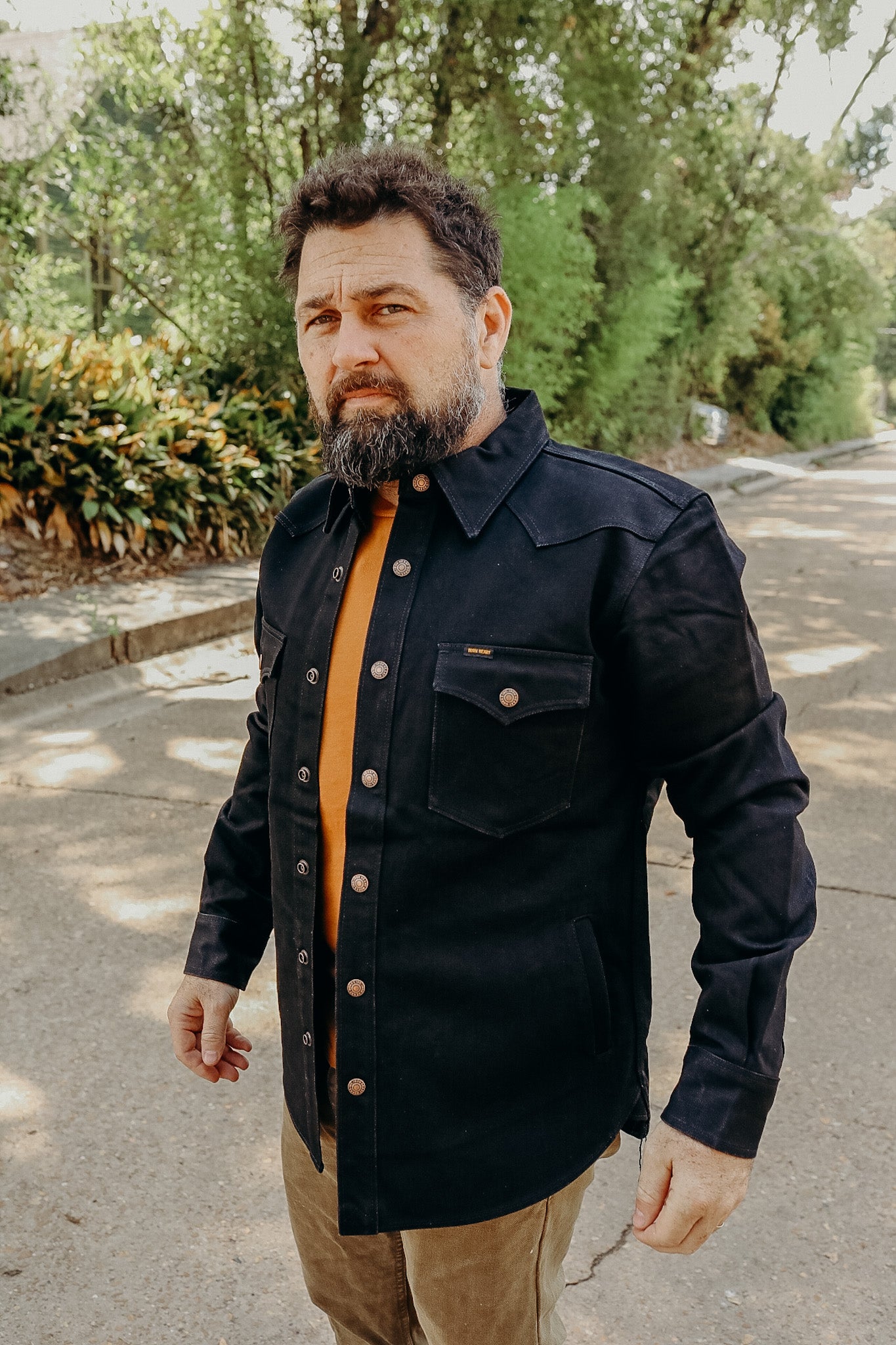 man with beard wearing black rugged work jacket and brown pants outdoors on sunny road