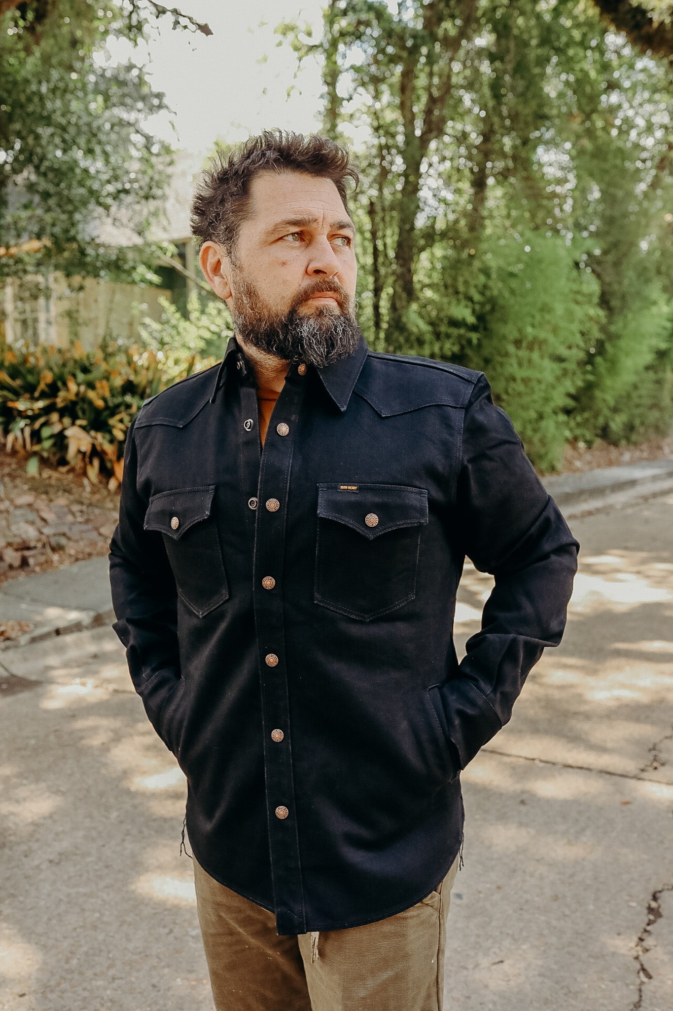 Man wearing black heavy-duty work shirt with buttons, standing outdoors on a sunny street