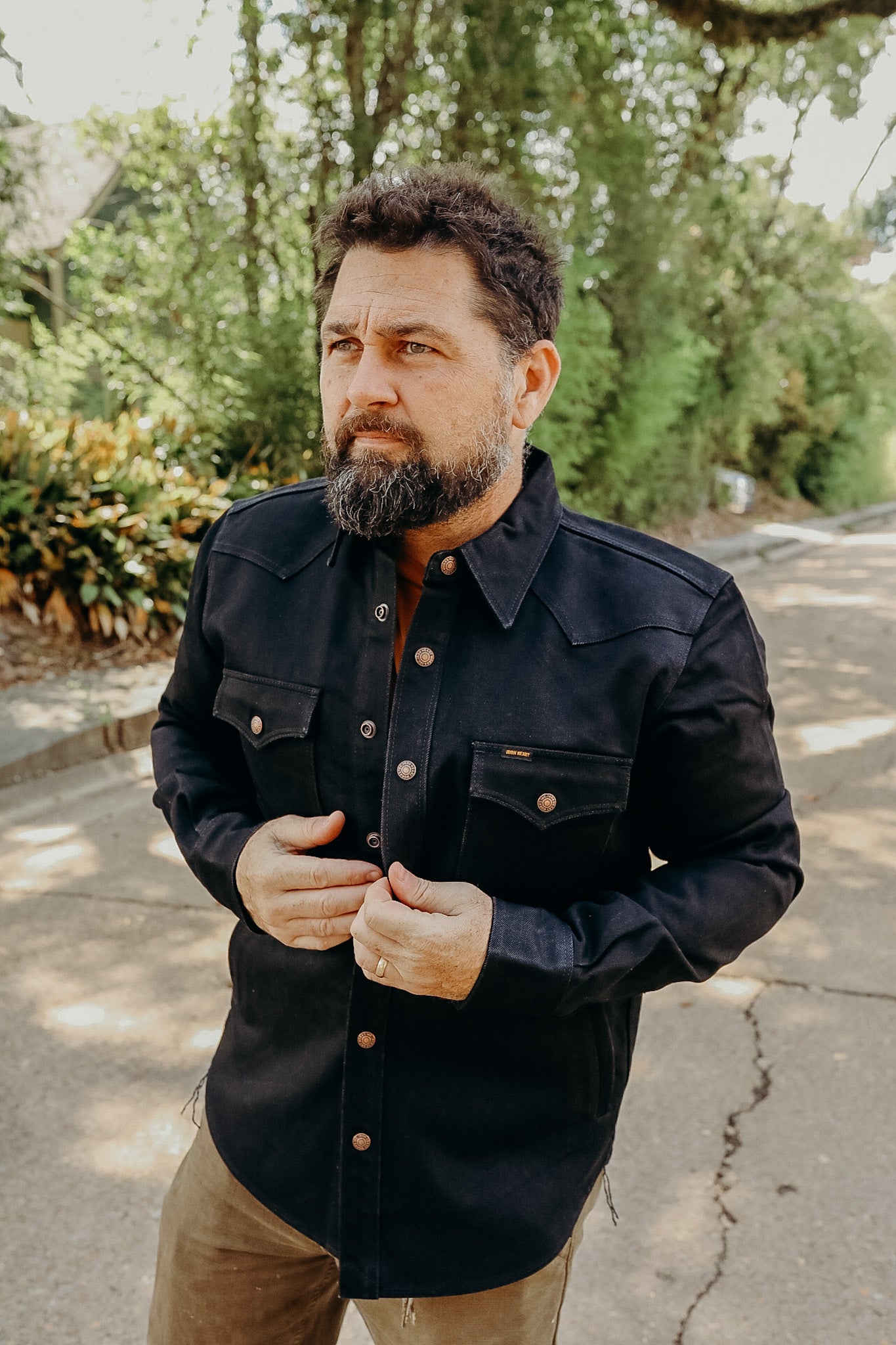 Man with beard wearing black heavy-duty shirt jacket with metal buttons outdoors on sunny day