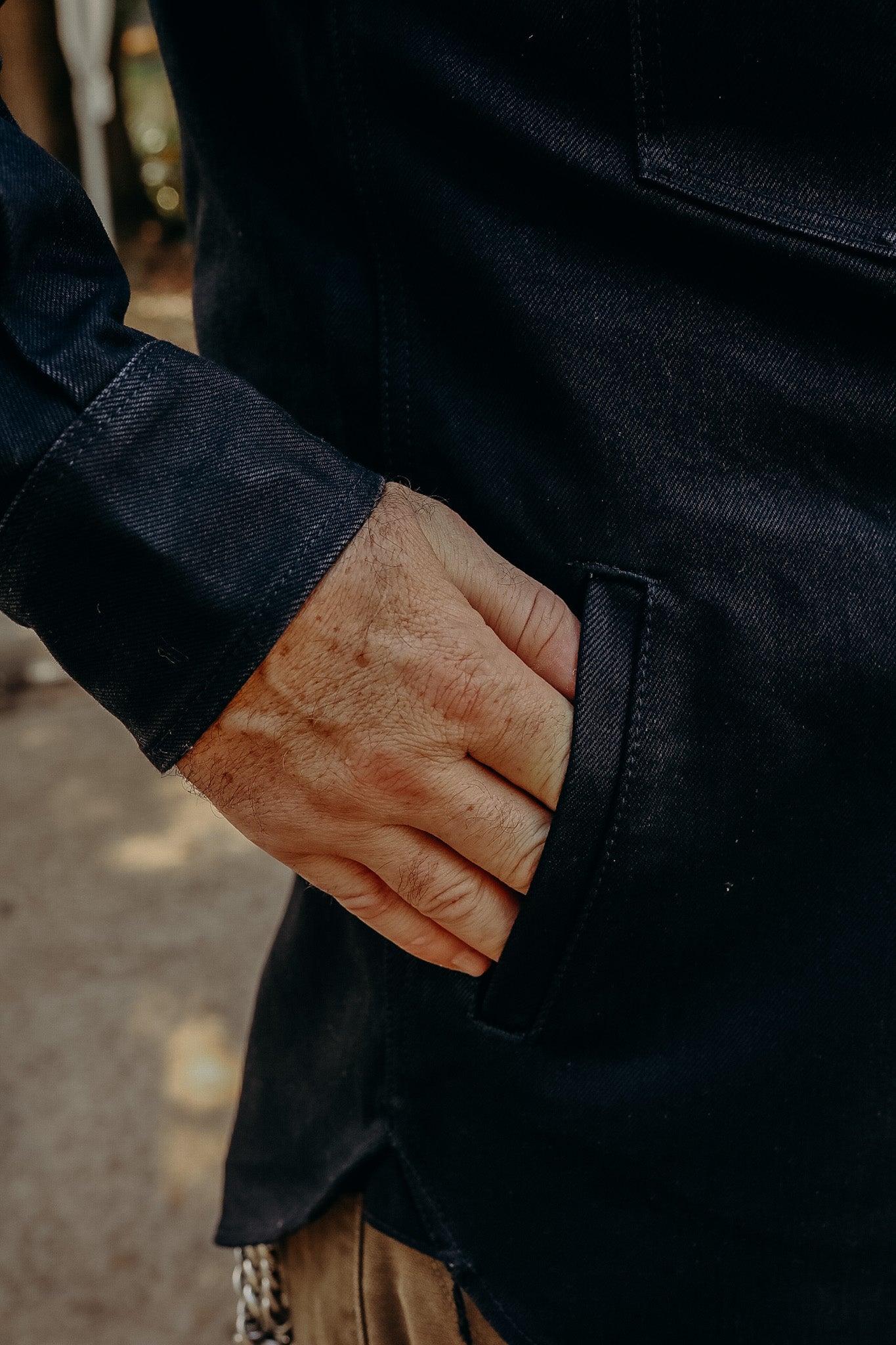 Close-up of hand in pocket of dark denim jacket, showcasing durable ironwork style clothing