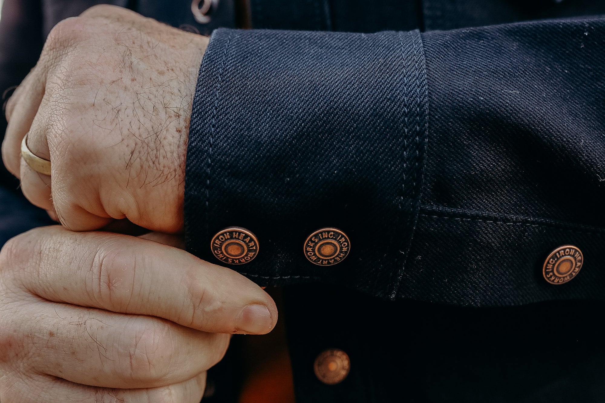 Close-up of hands adjusting dark denim shirt cuff with copper Iron Heart branded buttons