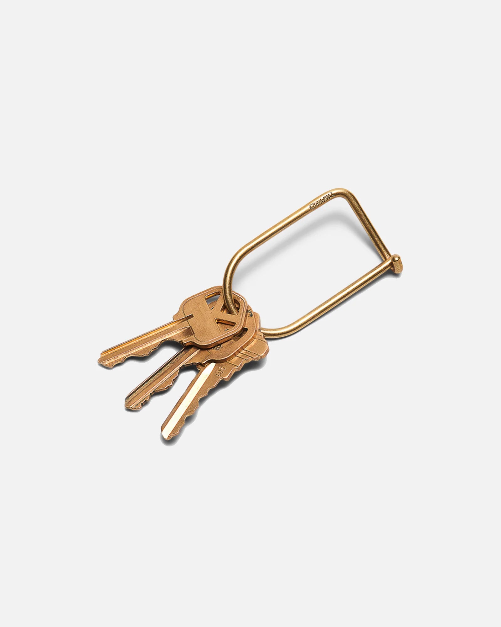 Three brass keys on a rectangular brass keyring against white background, Iron Shop Provisions style