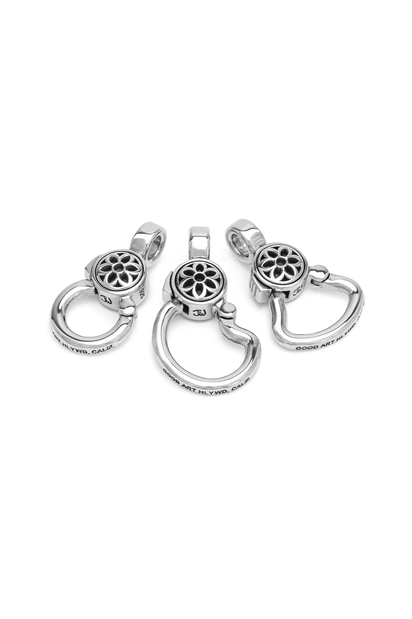 Three silver metal pendant charms with floral cutout designs and engraved text, isolated on white