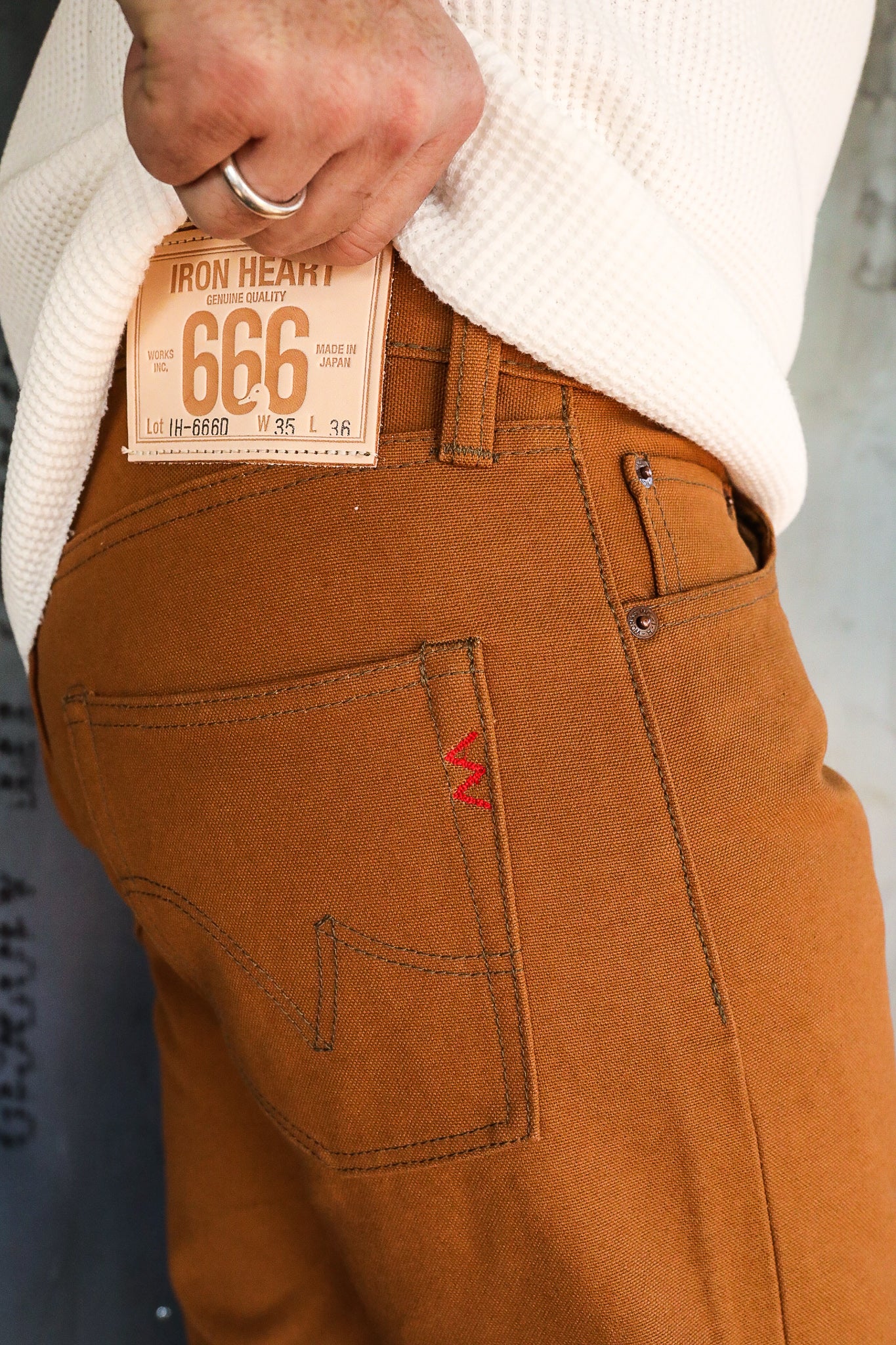 Close-up of person wearing brown Iron Heart IH-666D work pants with leather brand patch and white textured sweater