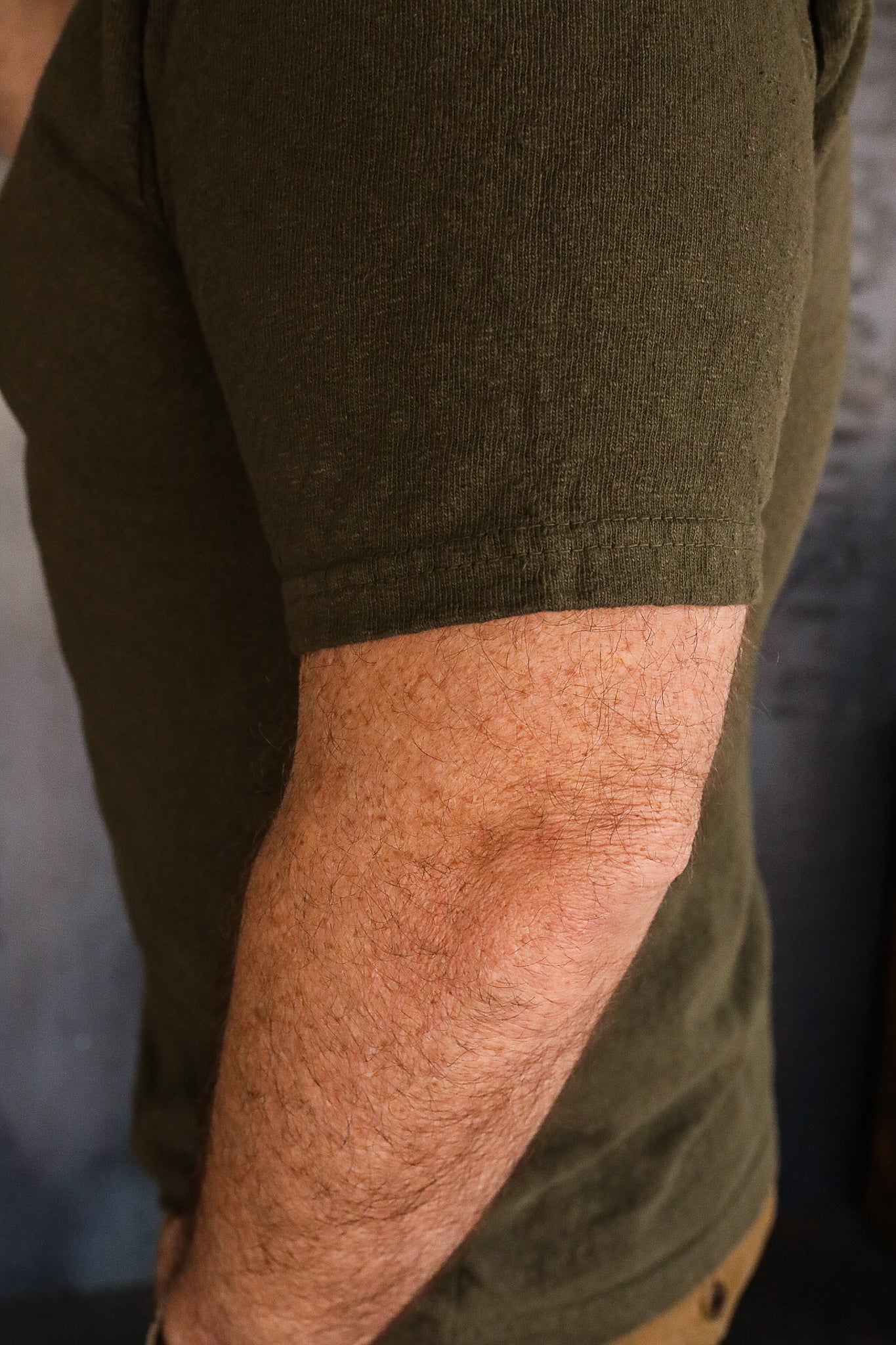 Close-up of a man's arm wearing an olive green short-sleeve shirt from Iron Shop Provisions