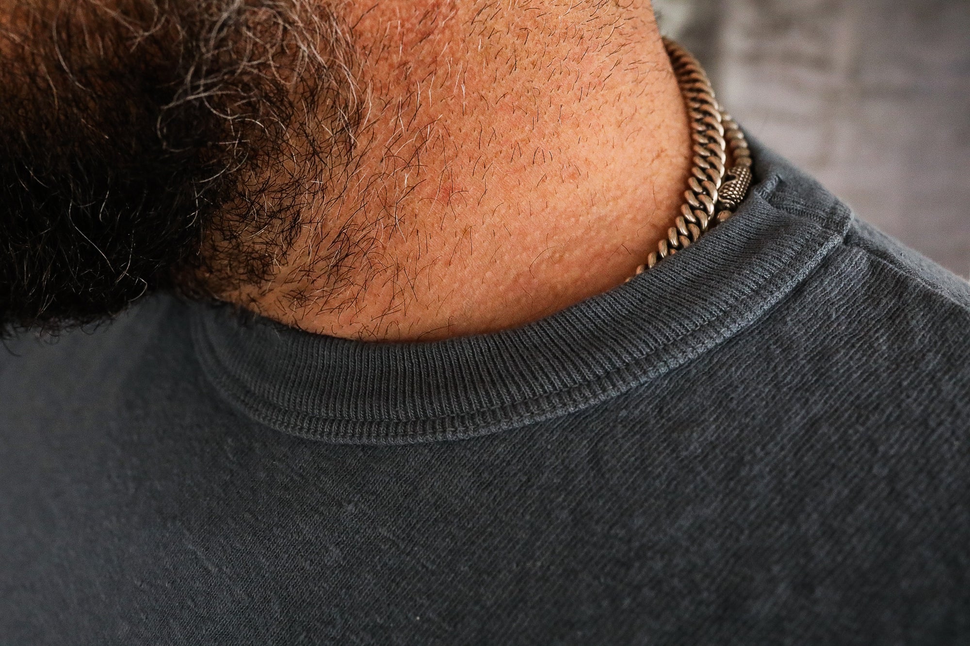 Close-up of man's neck wearing a textured silver chain necklace and a dark grey cotton shirt