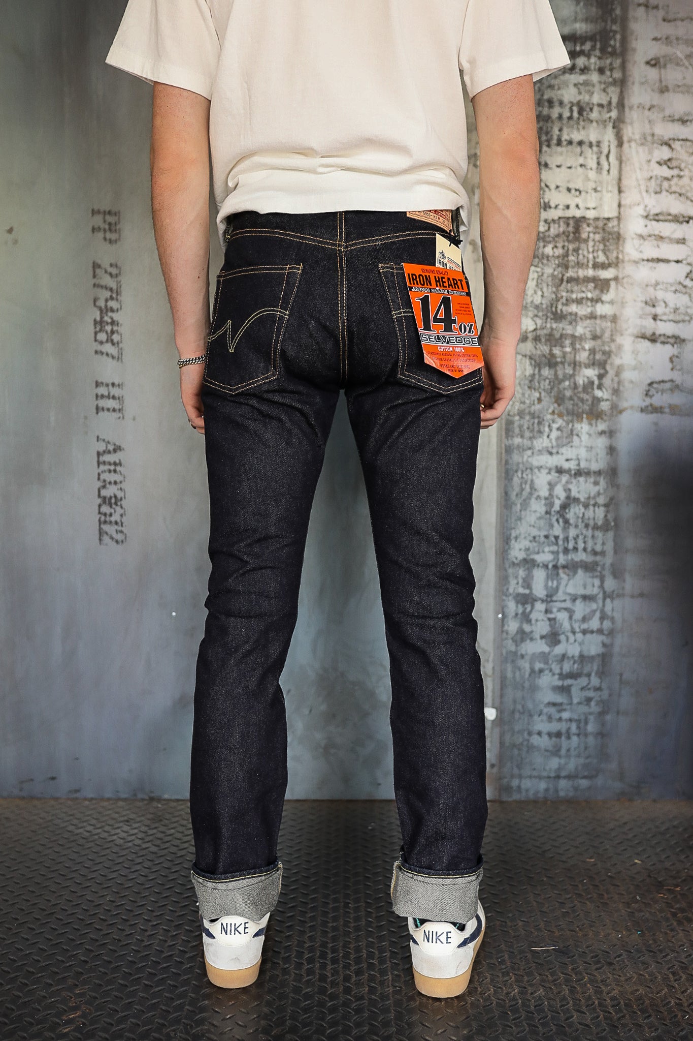 Back view of person wearing dark Iron Heart 14oz selvage denim jeans and white Nike sneakers on industrial floor