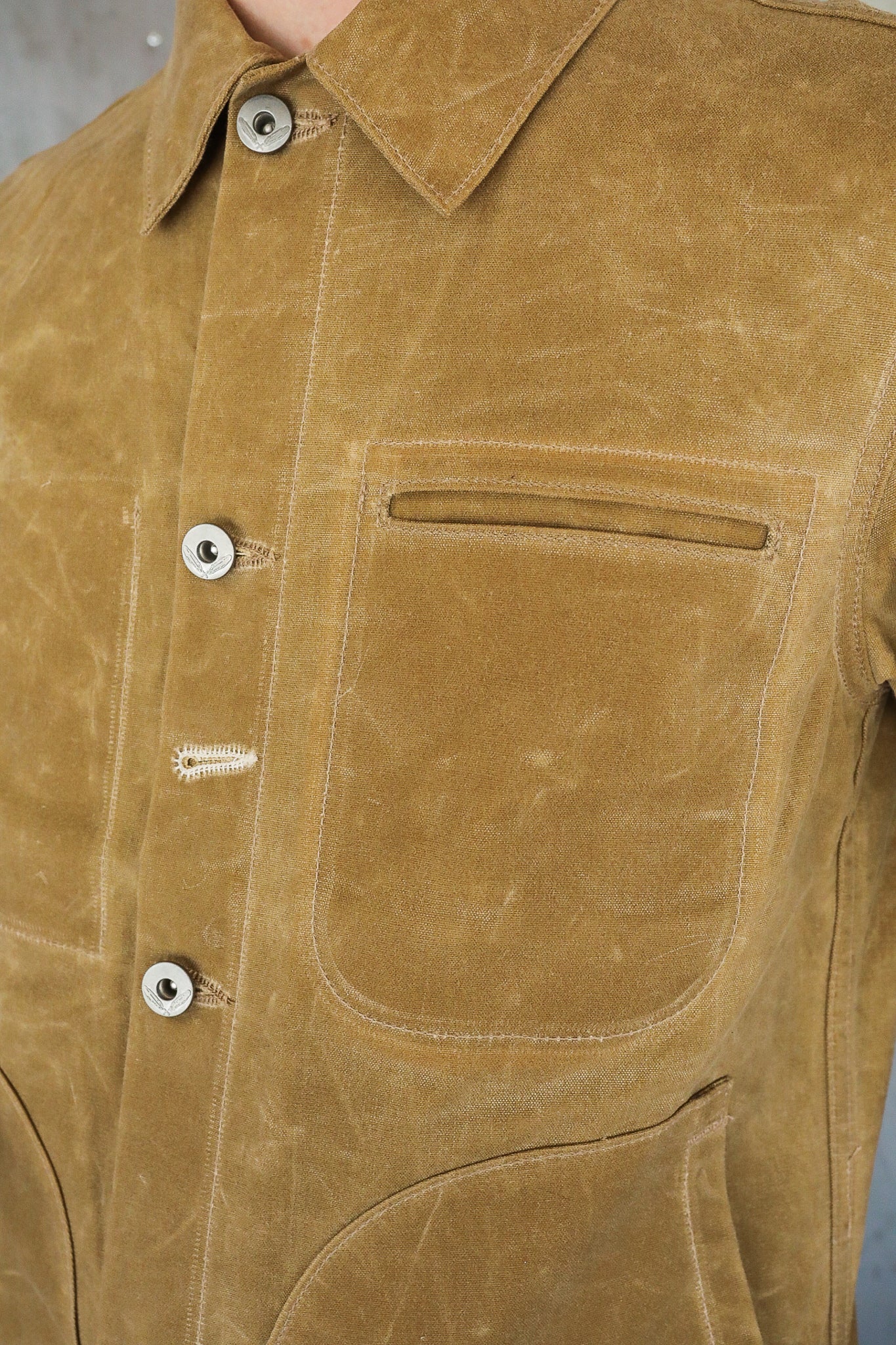 Close-up of brown waxed canvas worker jacket with silver buttons and chest pocket from Iron Shop Provisions