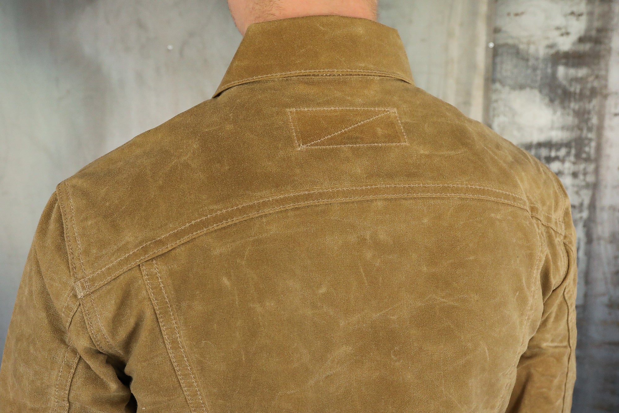 Back view of a brown waxed canvas jacket with double stitch detailing on the shoulders