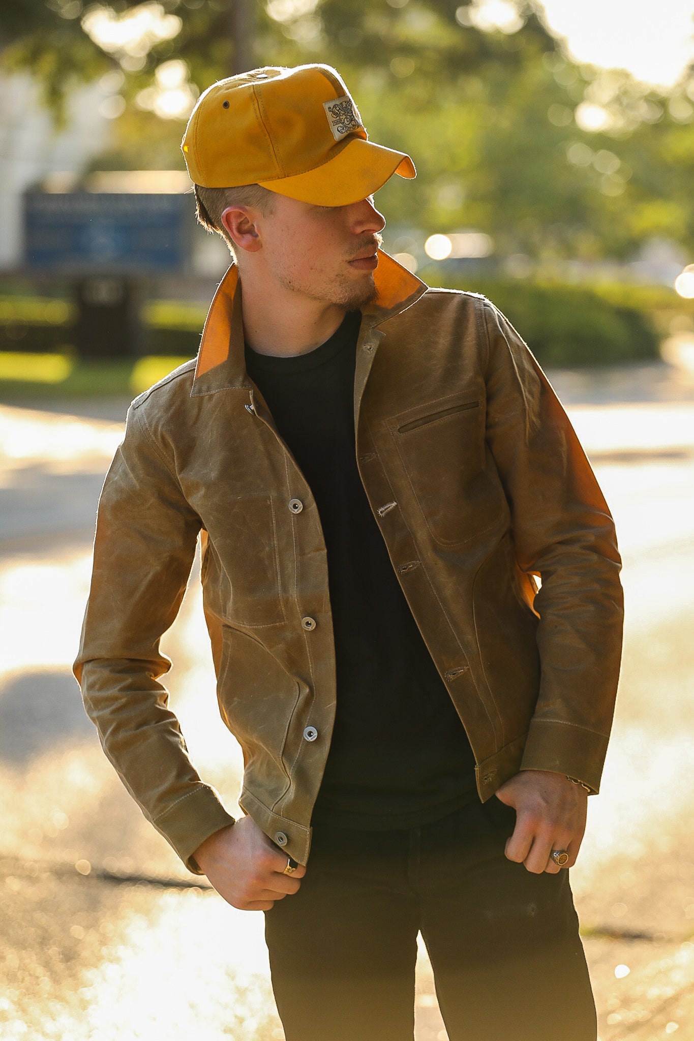 Man wearing a tan rugged jacket and mustard yellow cap outdoors in soft sunlight