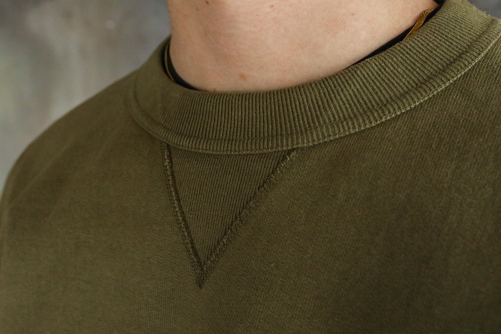 Close-up of olive green crewneck sweatshirt collar with triangular stitch detail, worn by person