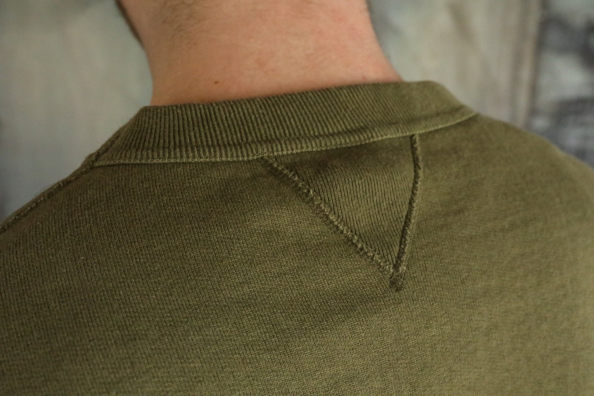 Close-up of olive green knit sweater back shoulder detail with V-shaped stitch at neckline
