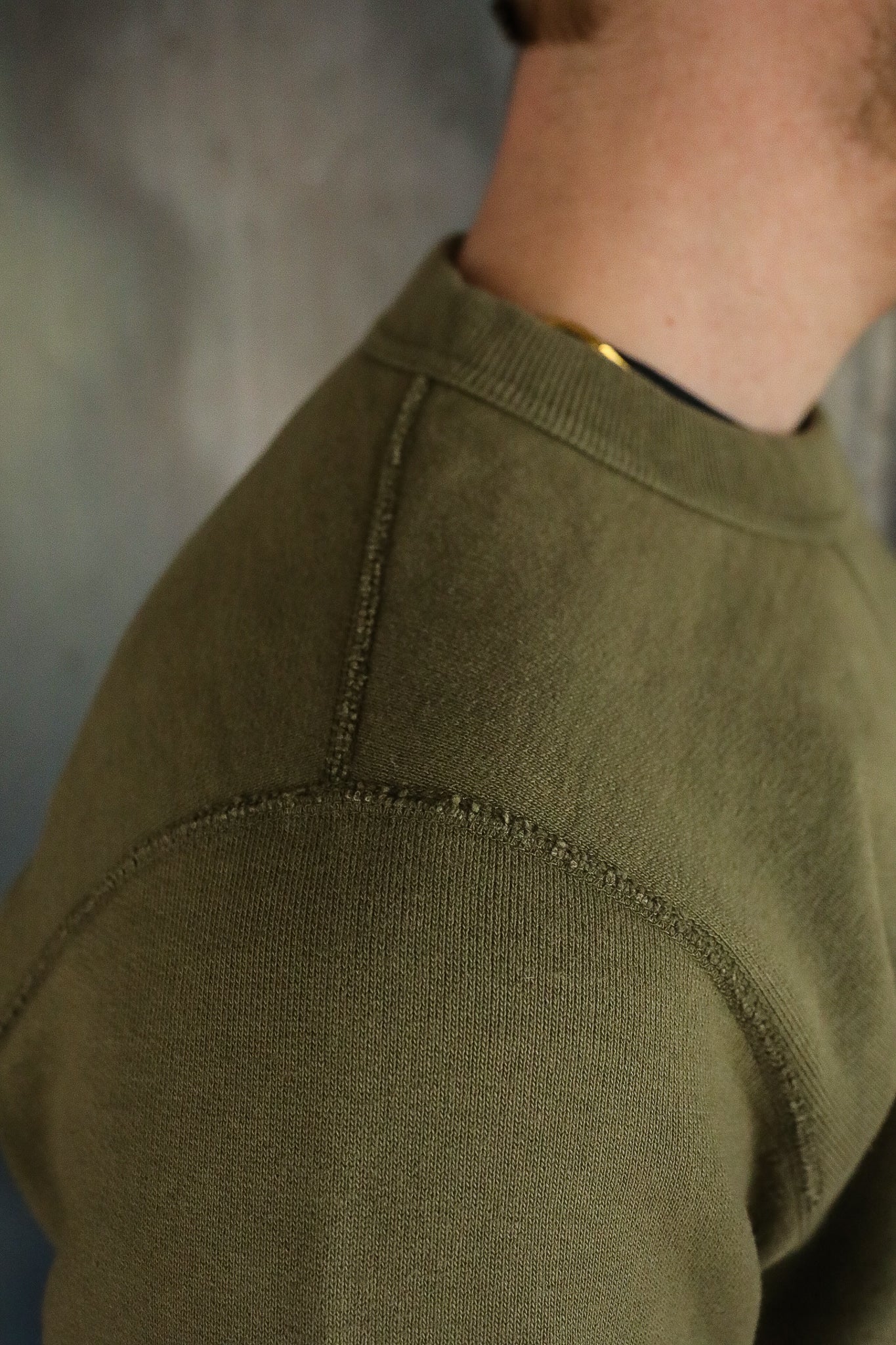 Close-up of olive green sweatshirt shoulder with detailed stitching and ribbed collar
