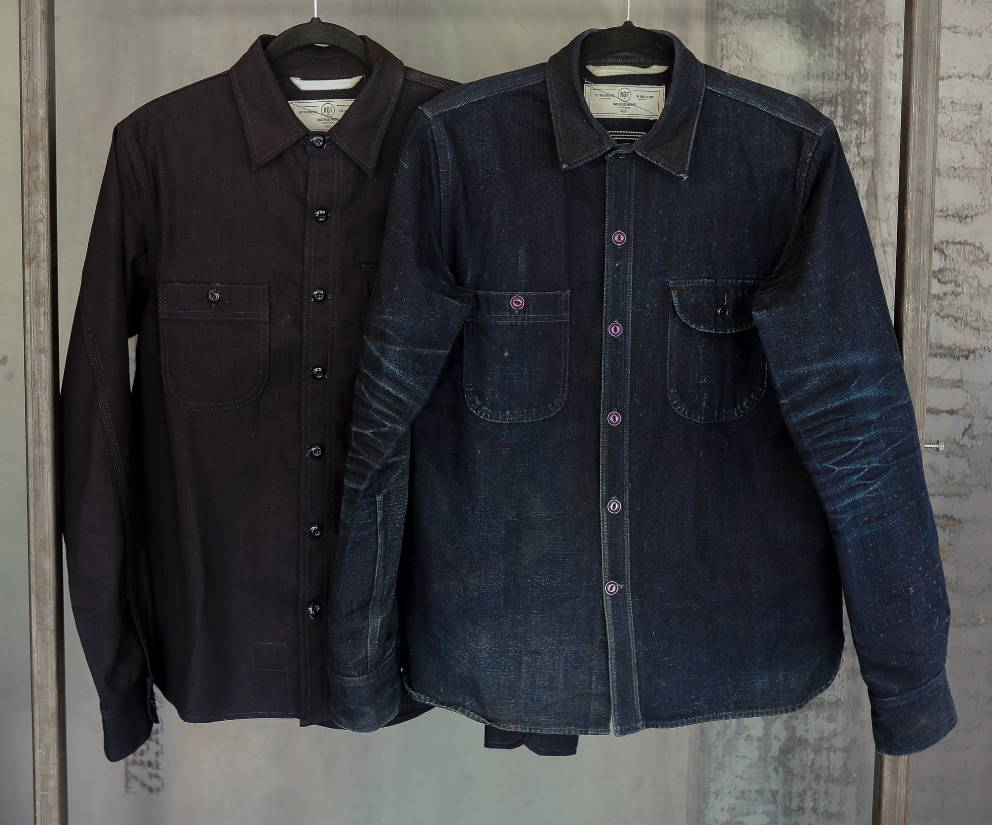 Two long-sleeve button-up shirts hanging on metal rack, one dark brown and one faded indigo denim