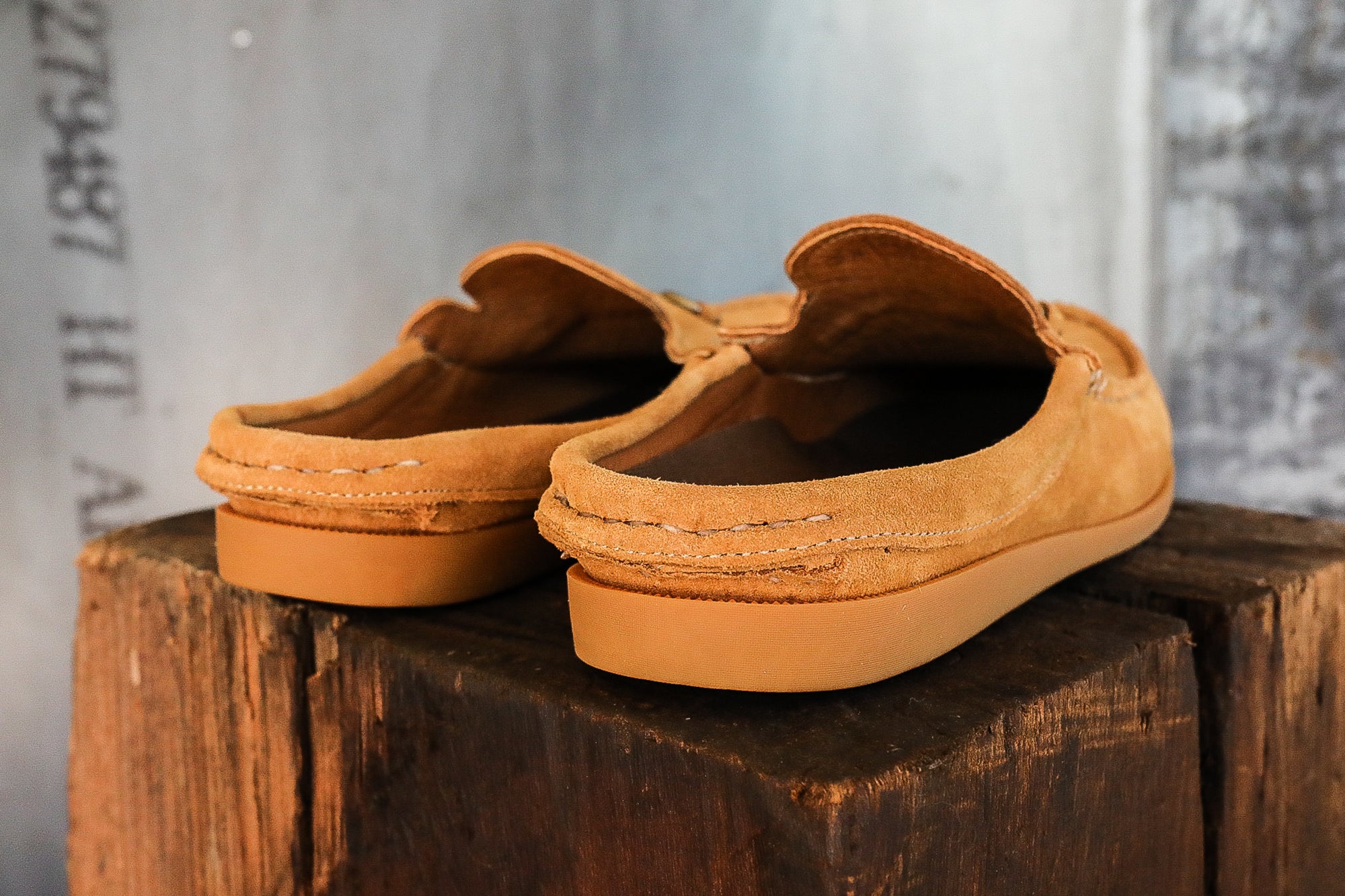 Pair of tan suede slip-on loafers with rubber soles on rustic wooden block
