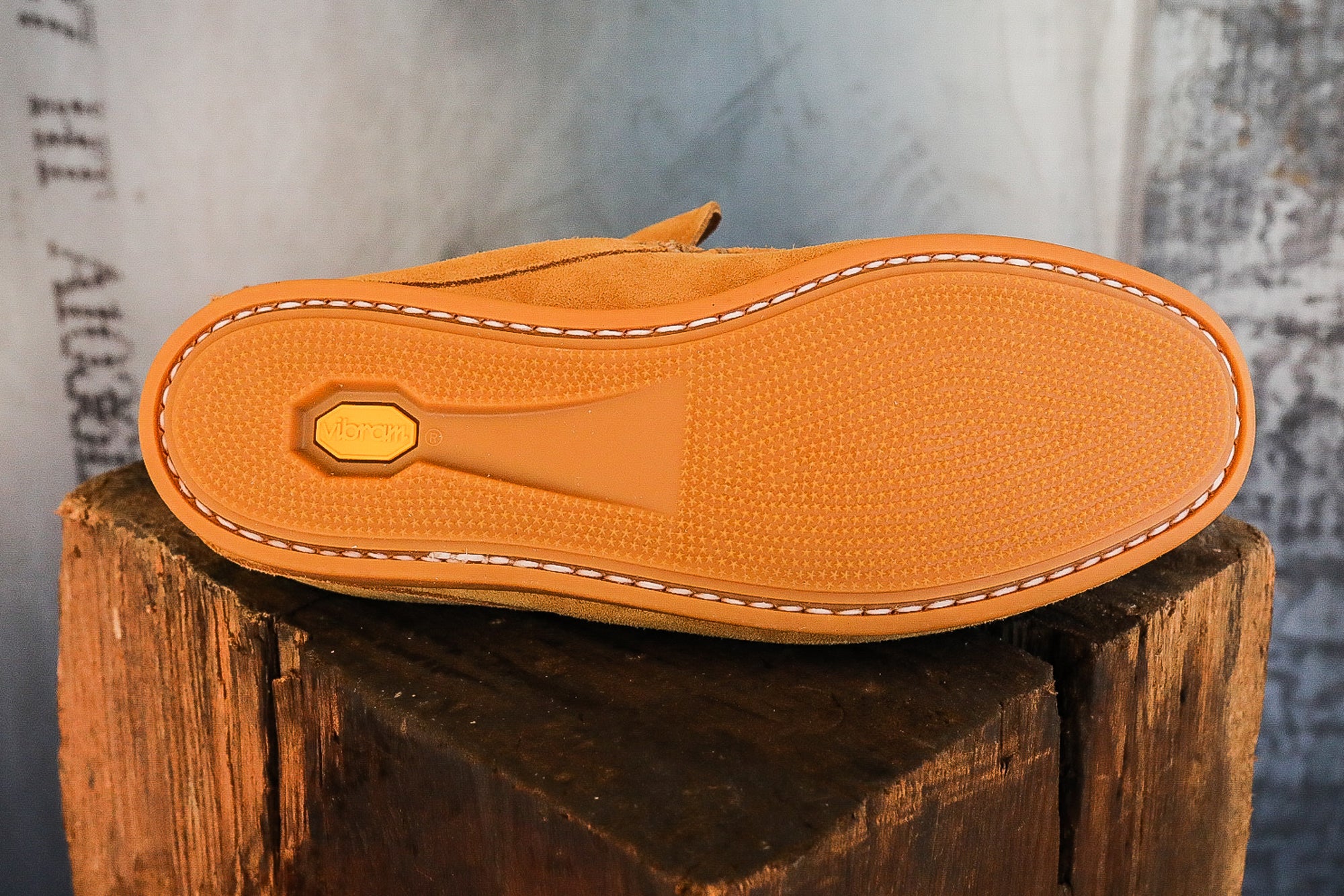 Bottom view of tan suede shoe with Vibram rubber sole and white stitching on wooden block