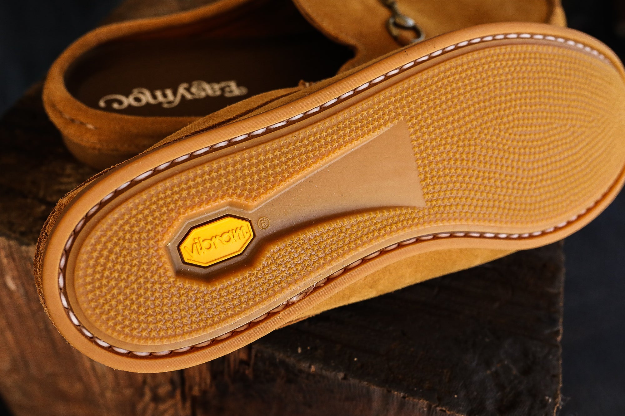 Close-up of Vibram sole on brown suede moccasin shoes resting on wooden surface
