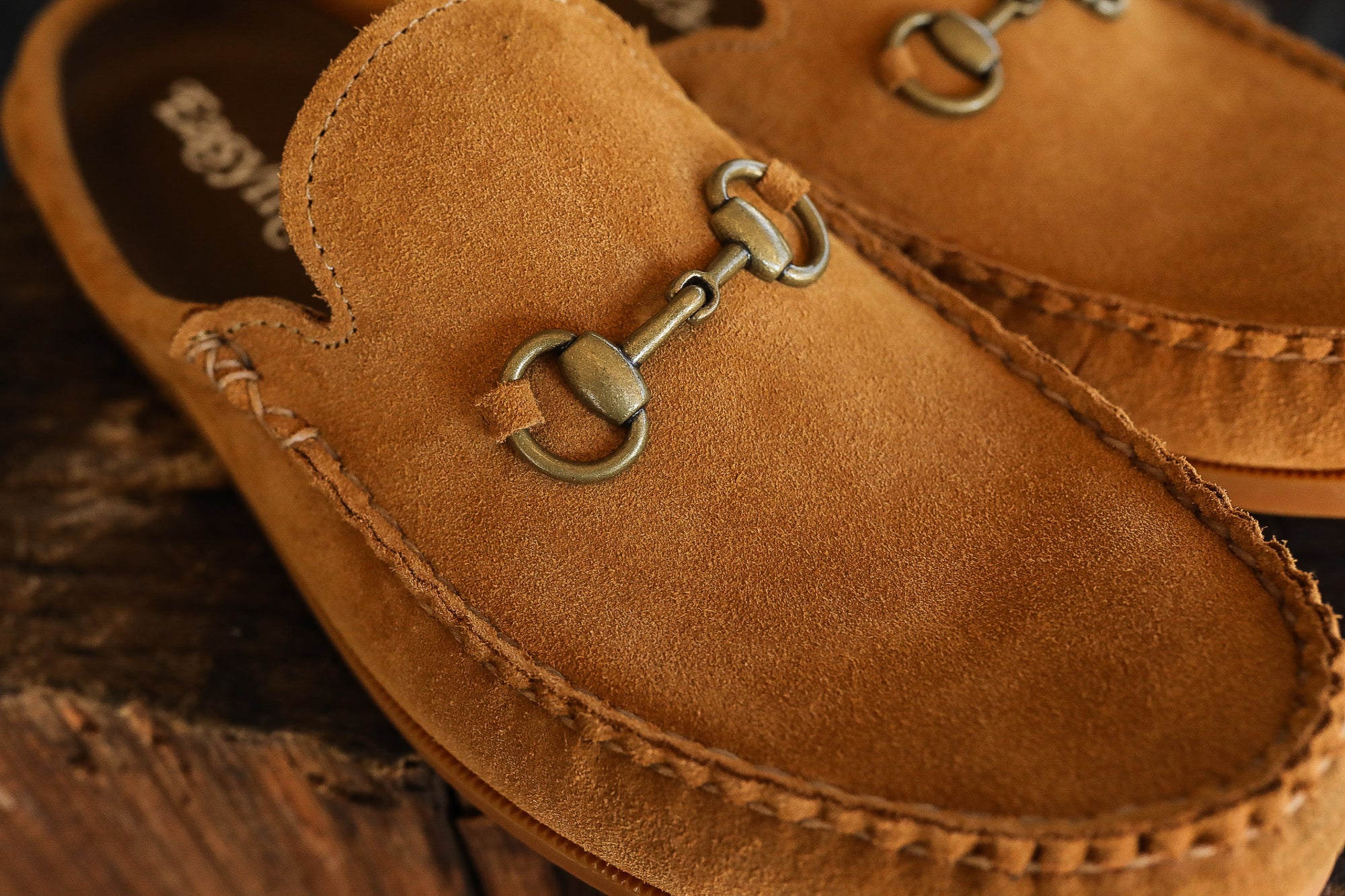 Close-up of tan suede loafers with metal horsebit detail on wooden surface