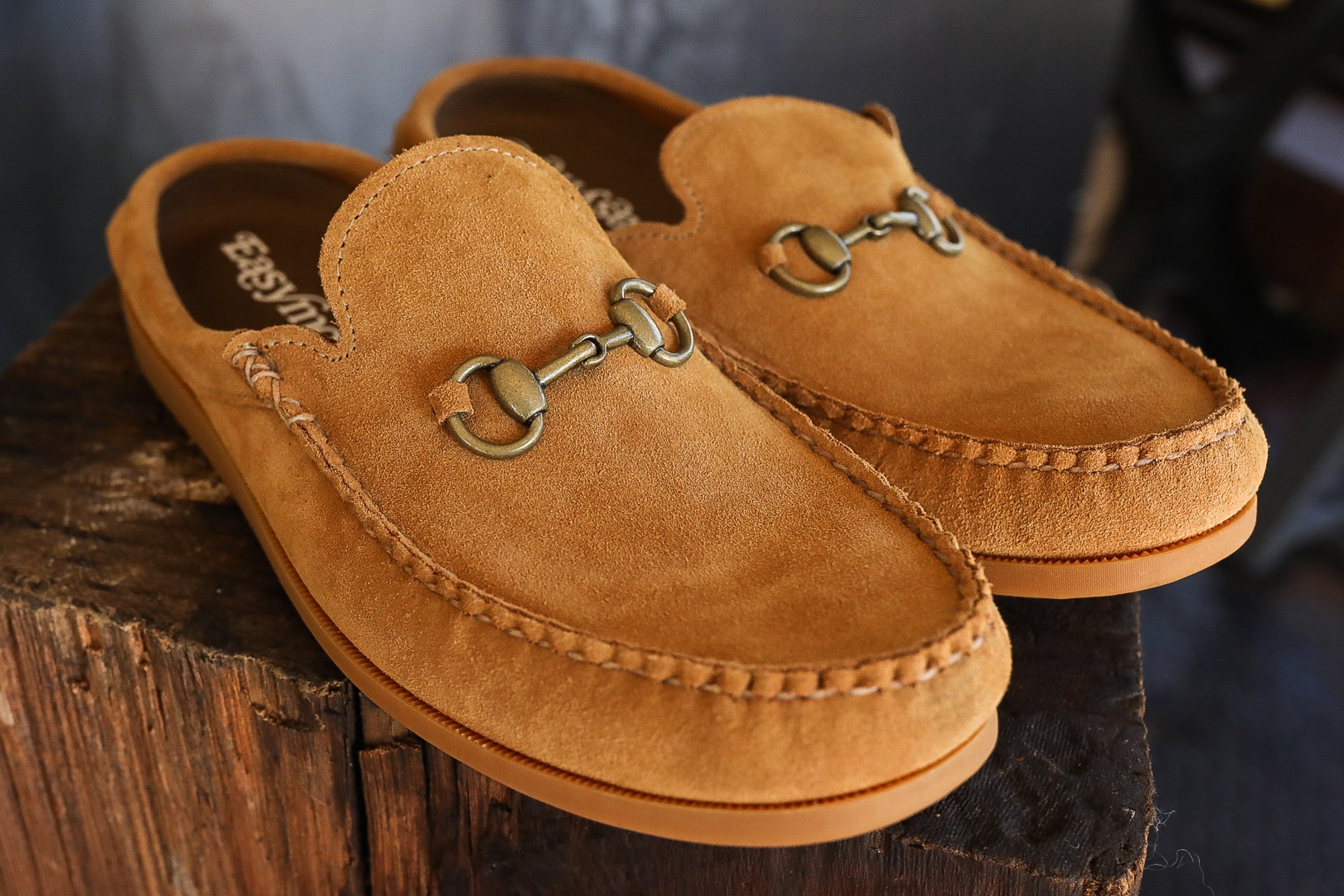 Pair of tan suede loafers with metal horsebit detail on rustic wooden surface