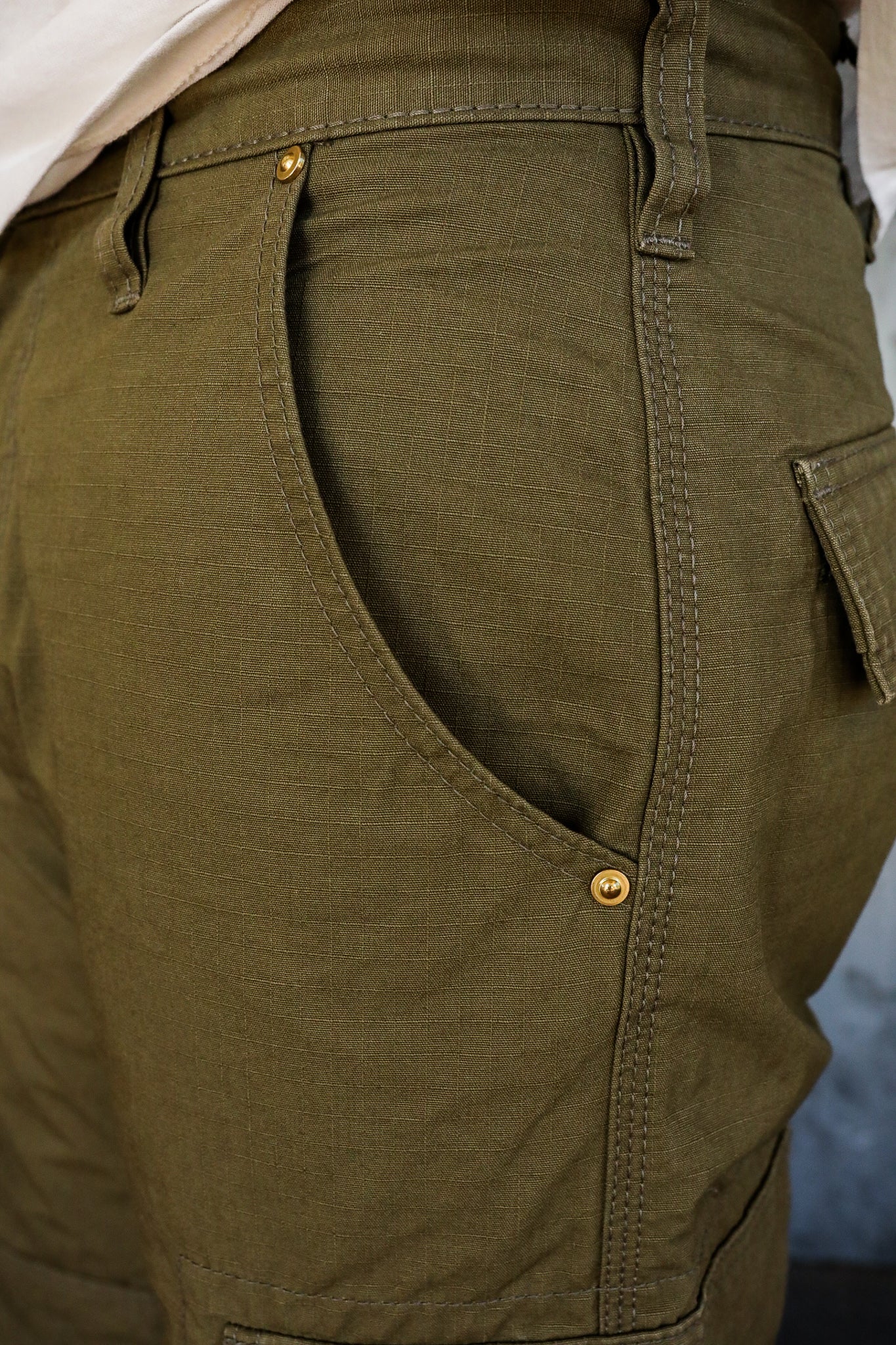 Close-up of olive green durable work pants pocket with reinforced stitching and brass rivets