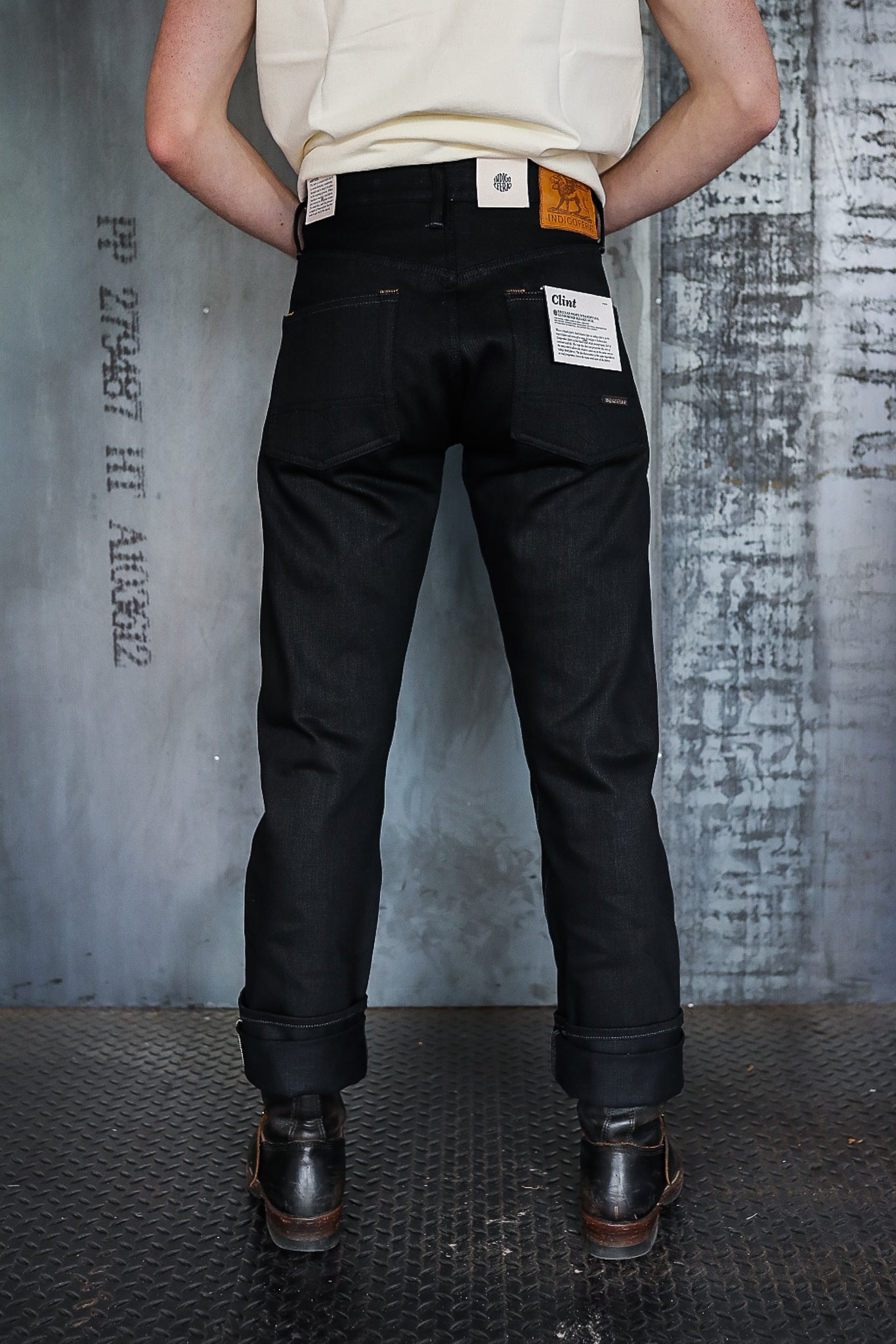 Back view of person wearing black denim jeans with folded cuffs and black leather boots on textured floor