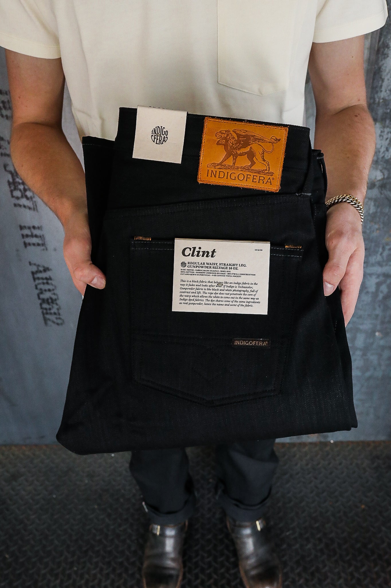 Person holding folded black Indigofera Clint jeans with leather logo patch and white label