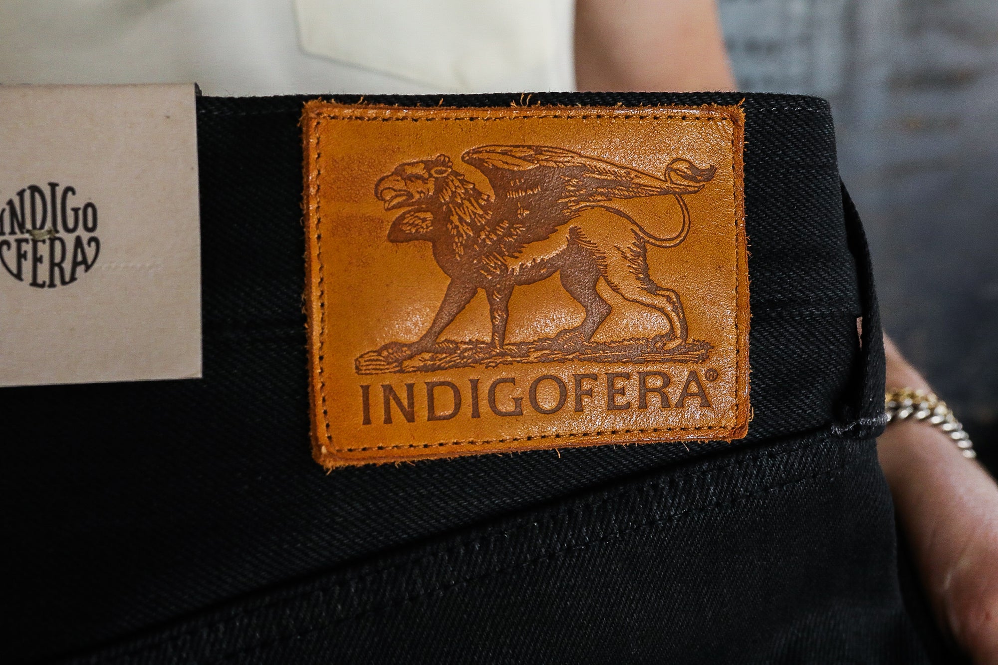 Indigofera black denim jeans with brown leather patch featuring griffin logo and Indigofera branding