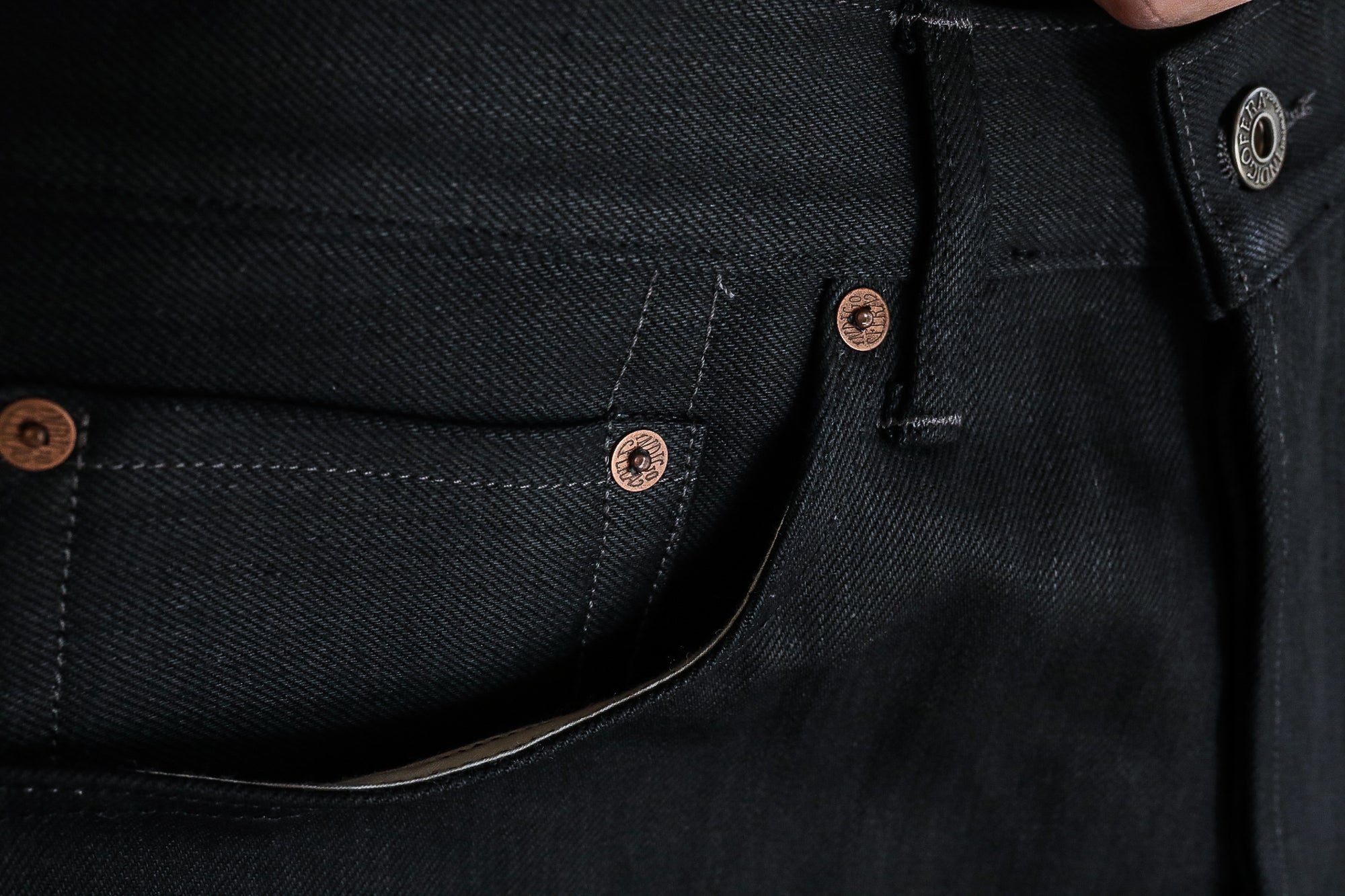 Close-up of black denim jeans pocket with copper rivets and metal button at waist