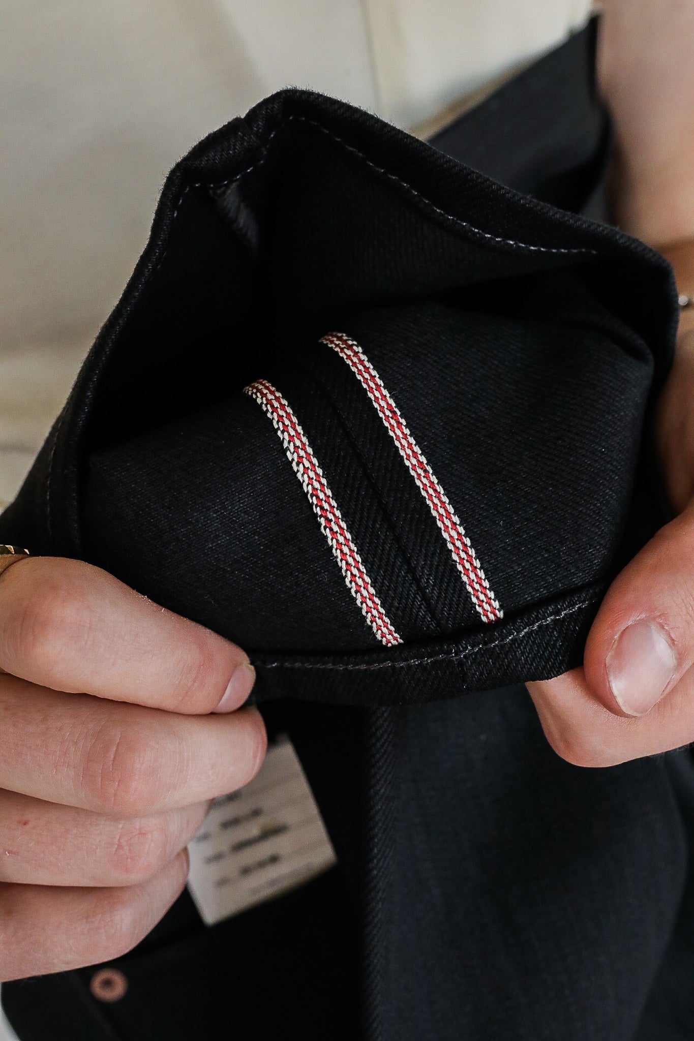 Close-up of hands holding black denim cuff showing red and white selvedge detail at Iron Shop Provisions