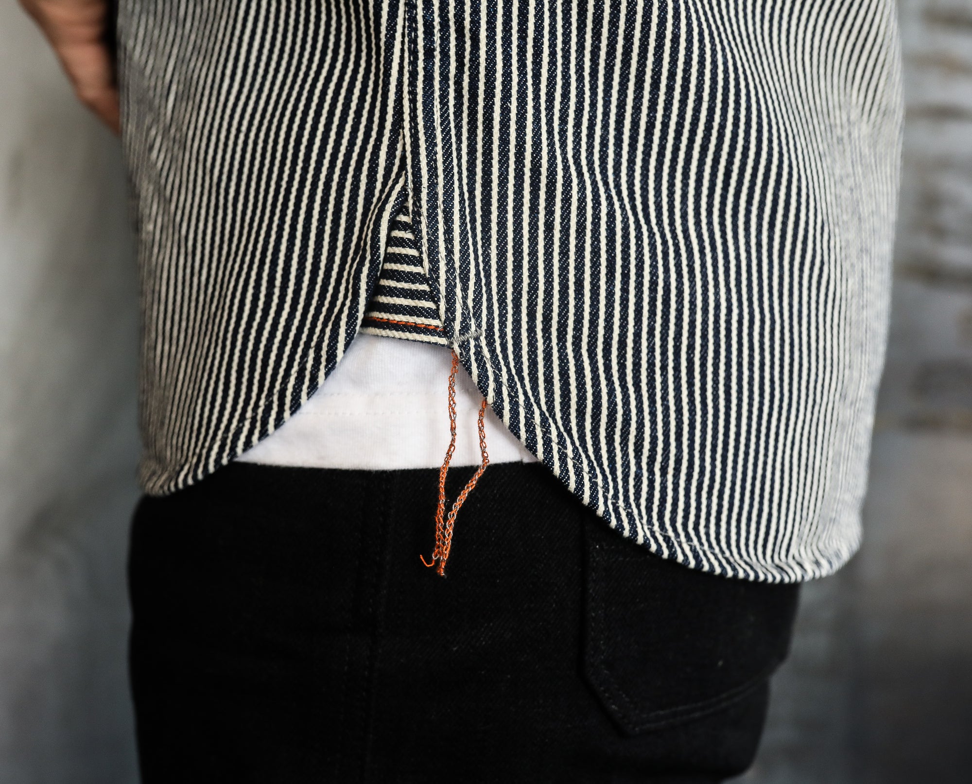 Close-up of striped shirt hem with orange loose thread over white undershirt and black pants
